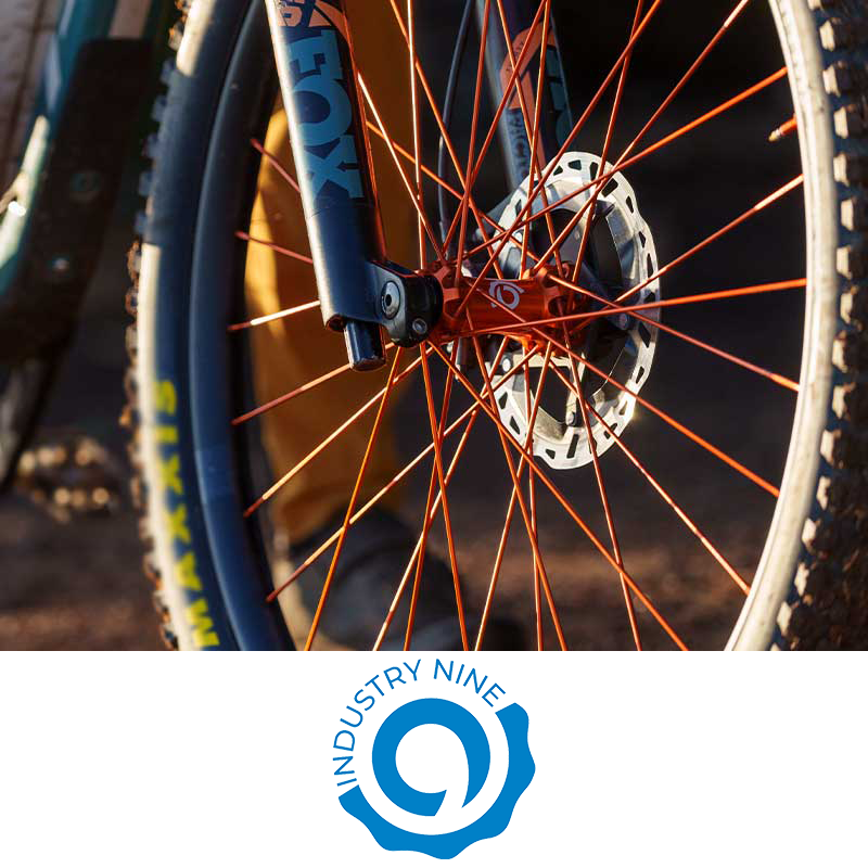Close-up of a mountain bike's front wheel with orange spokes, disc brake, and suspension fork.