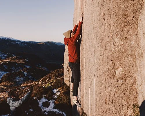 Person rock climbing outdoors with mountainous landscape in background.