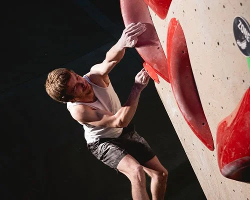 Person climbing an indoor bouldering wall with red holds in a gym.