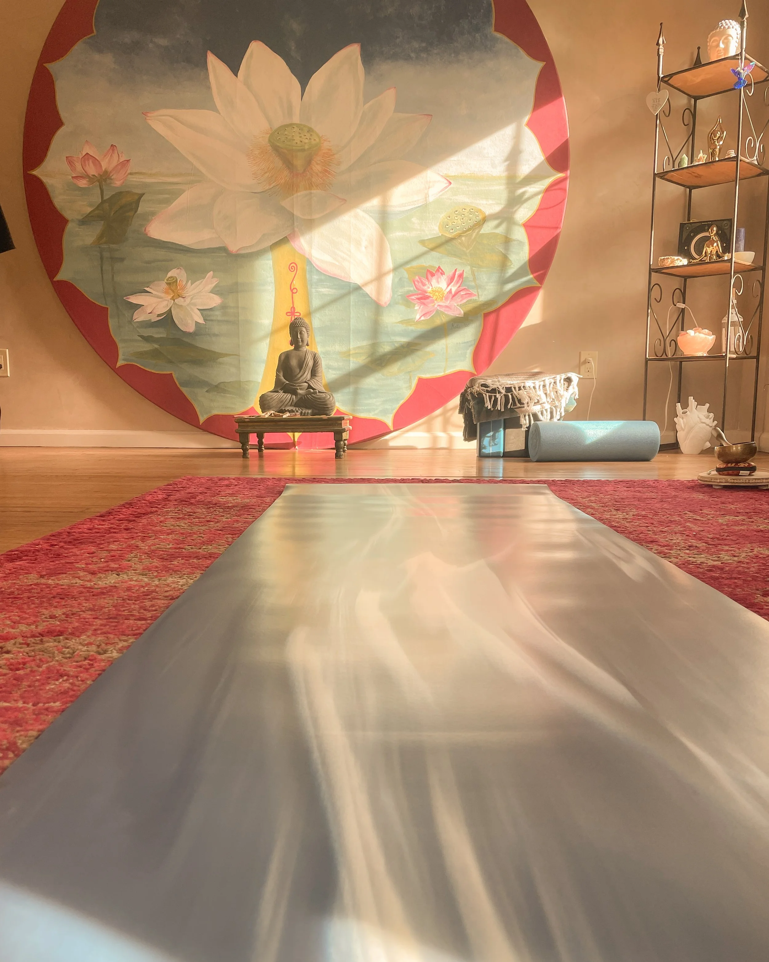 A peaceful room with a yoga mat on a rug, a Buddha statue, a lotus flower backdrop, and shelving with decorative items.