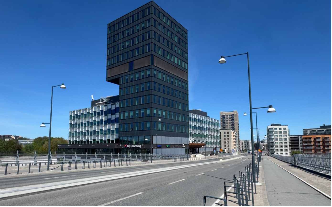 Modern office lounge with purple lighting, featuring a gray sofa with colorful cushions, poufs, plants, and a kitchenette in the background with a coffee machine. "Key Solutions" sign on the wall.