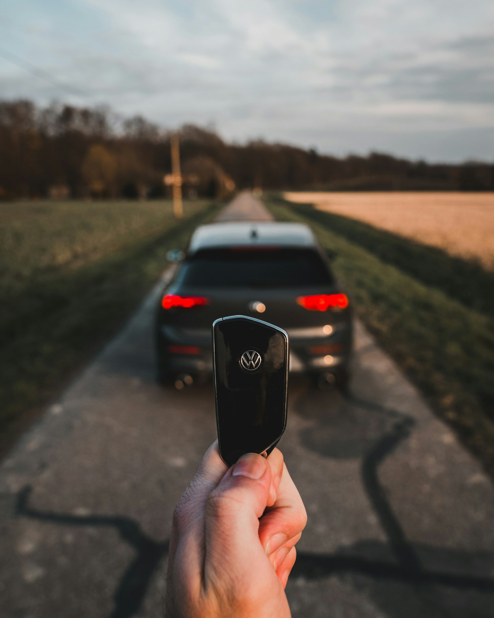 A hand holding a Volkswagen car key with a blurred Volkswagen car in the background on a rural road.