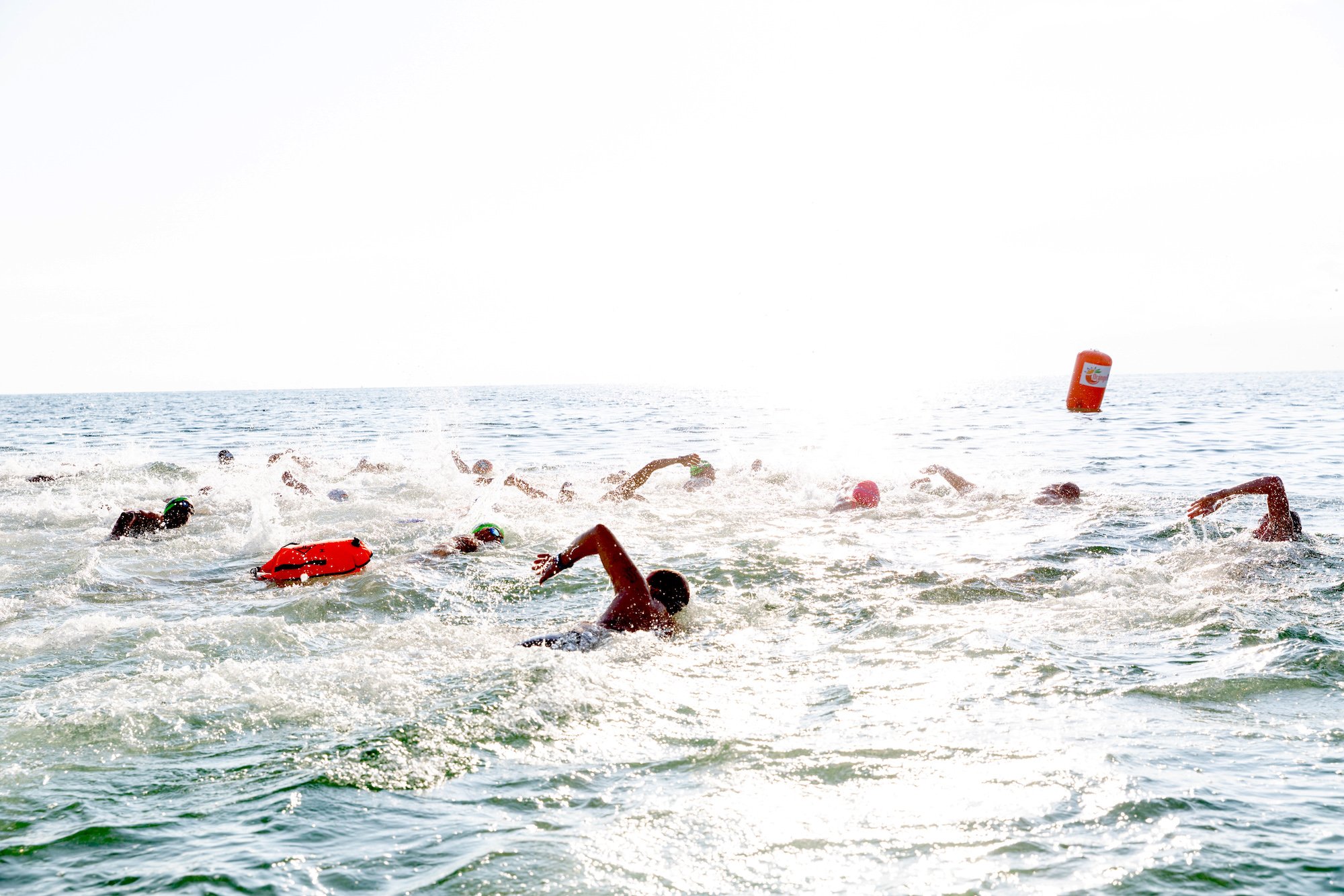 Group of swimmers in the ocean participating in an open water race, with orange buoy floating in the background.