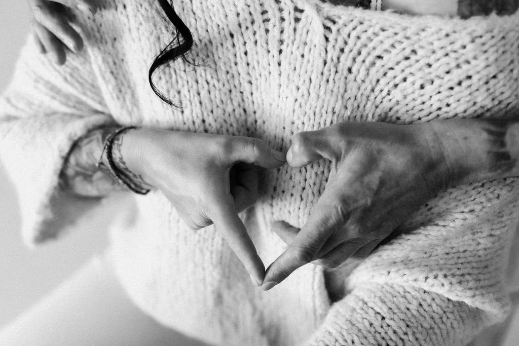 Zwei Hände formen ein Herz auf einem gestrickten Pullover.