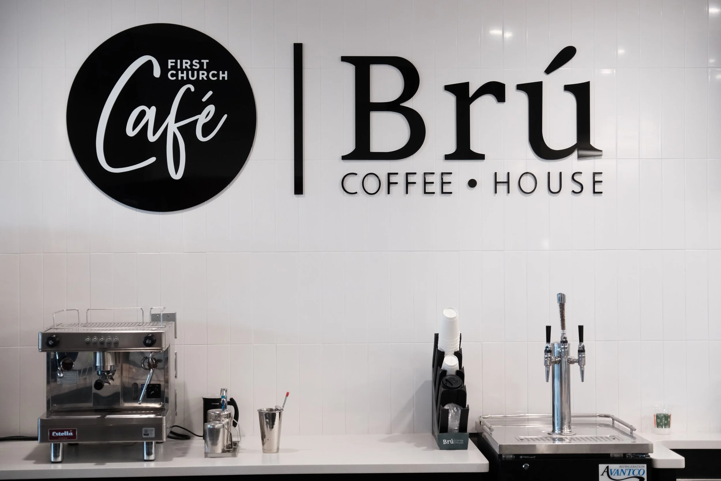 Coffee shop sign on a white wall that reads "Cafe, Bru Coffee House"