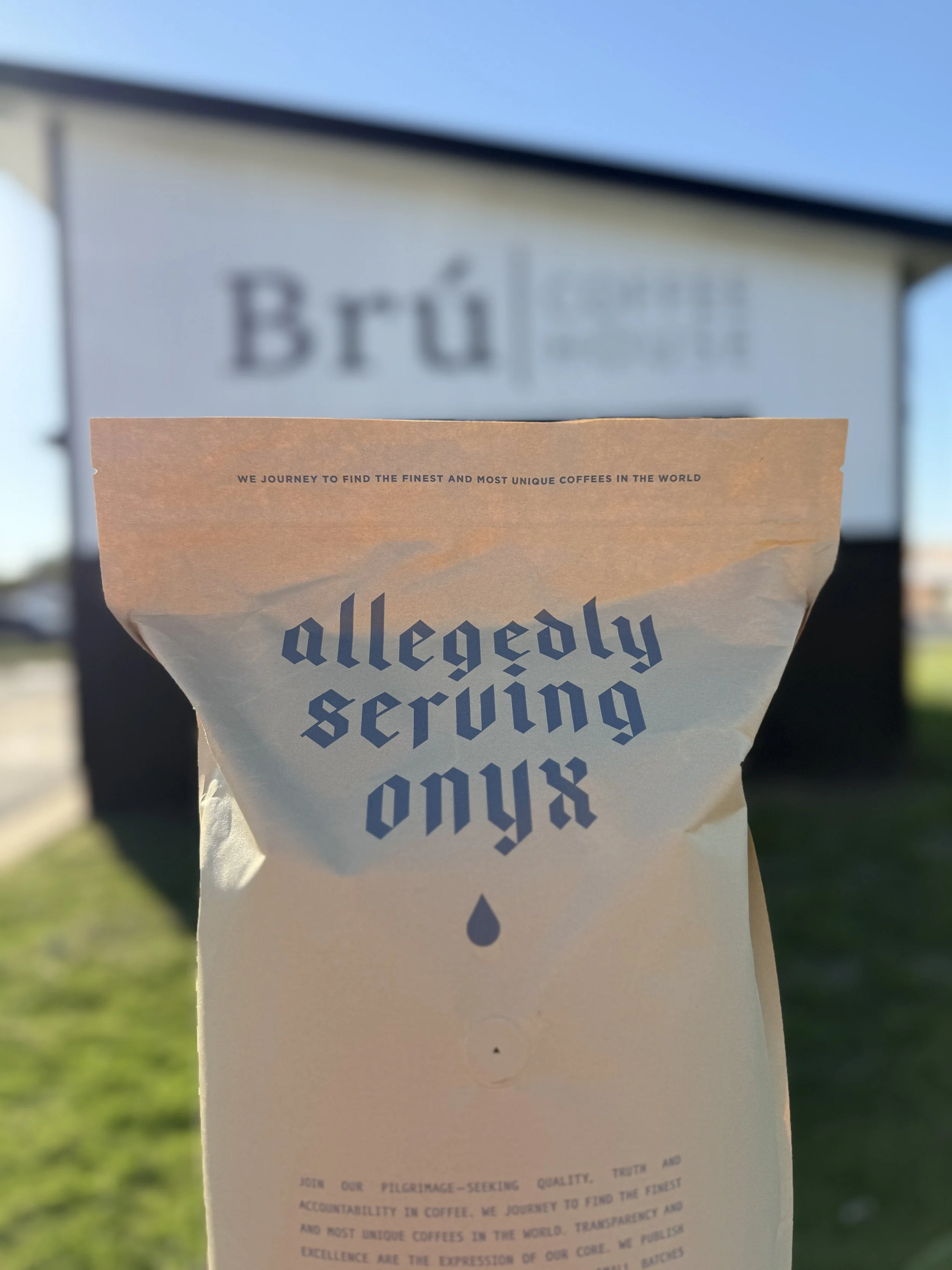 Bag of coffee that reads "Allegedly serving onyx" in front of a drive thru coffee trailer that reads "Bru Coffee House"