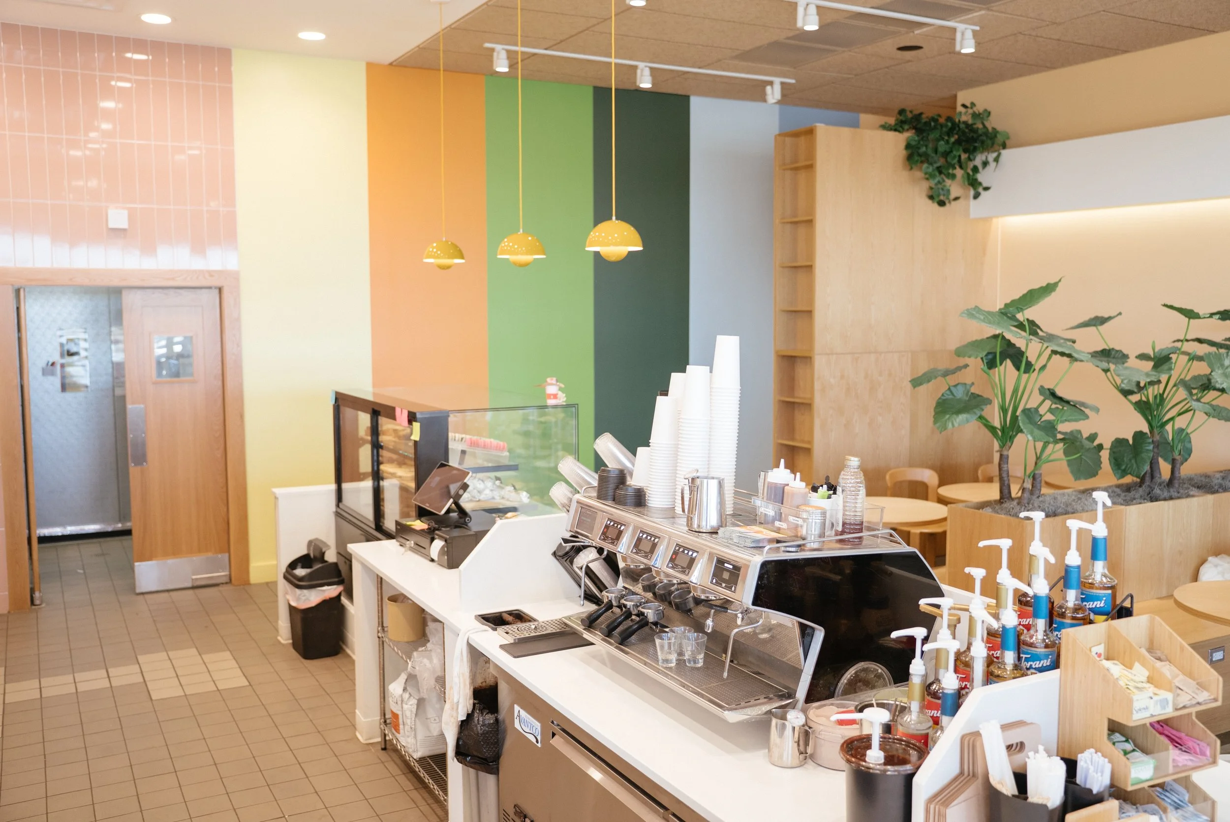 A colorful cafe interior with a counter, coffee machines, and green plants.