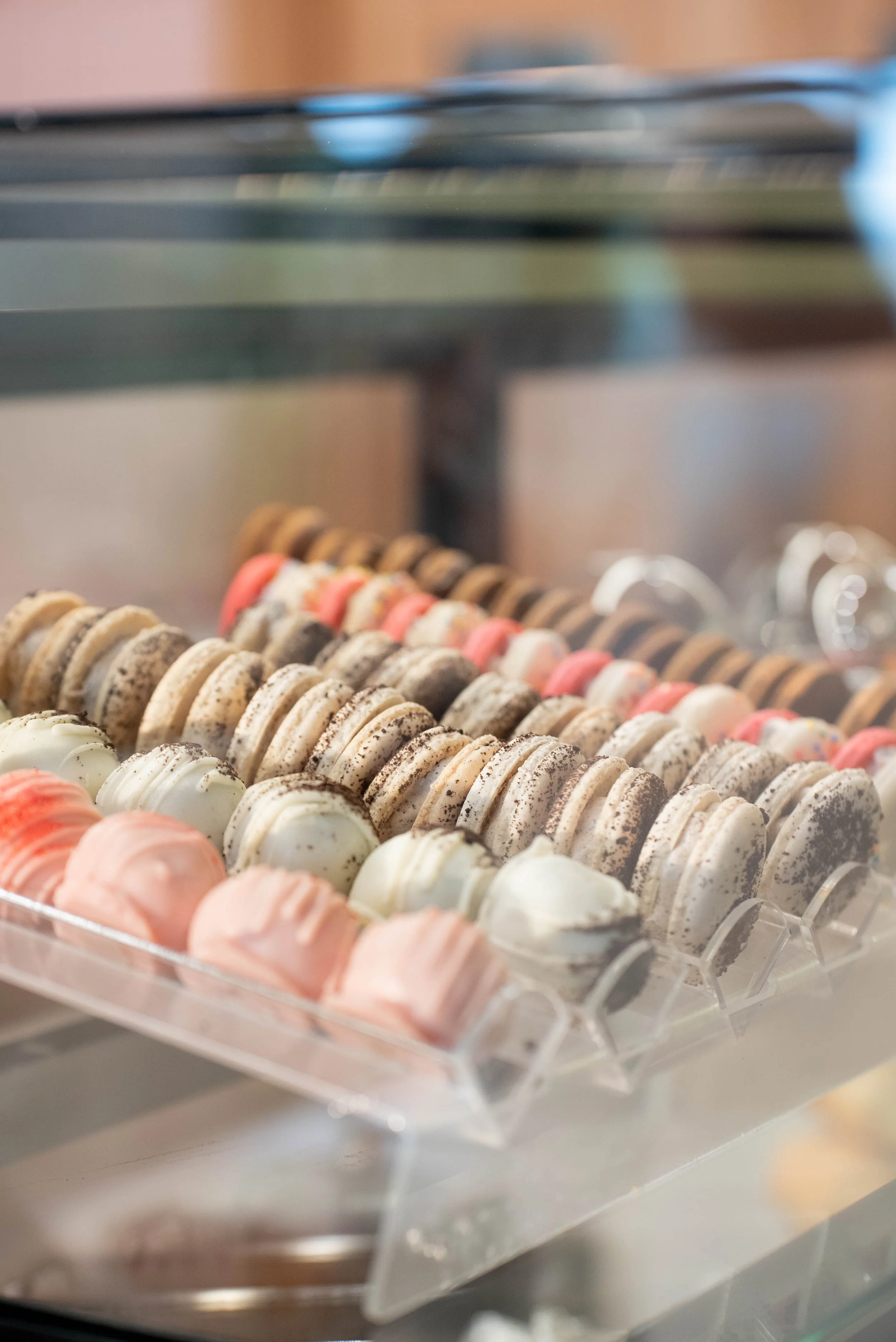 Display case filled with colorful macarons in pastel pink, green, white, brown, and beige.