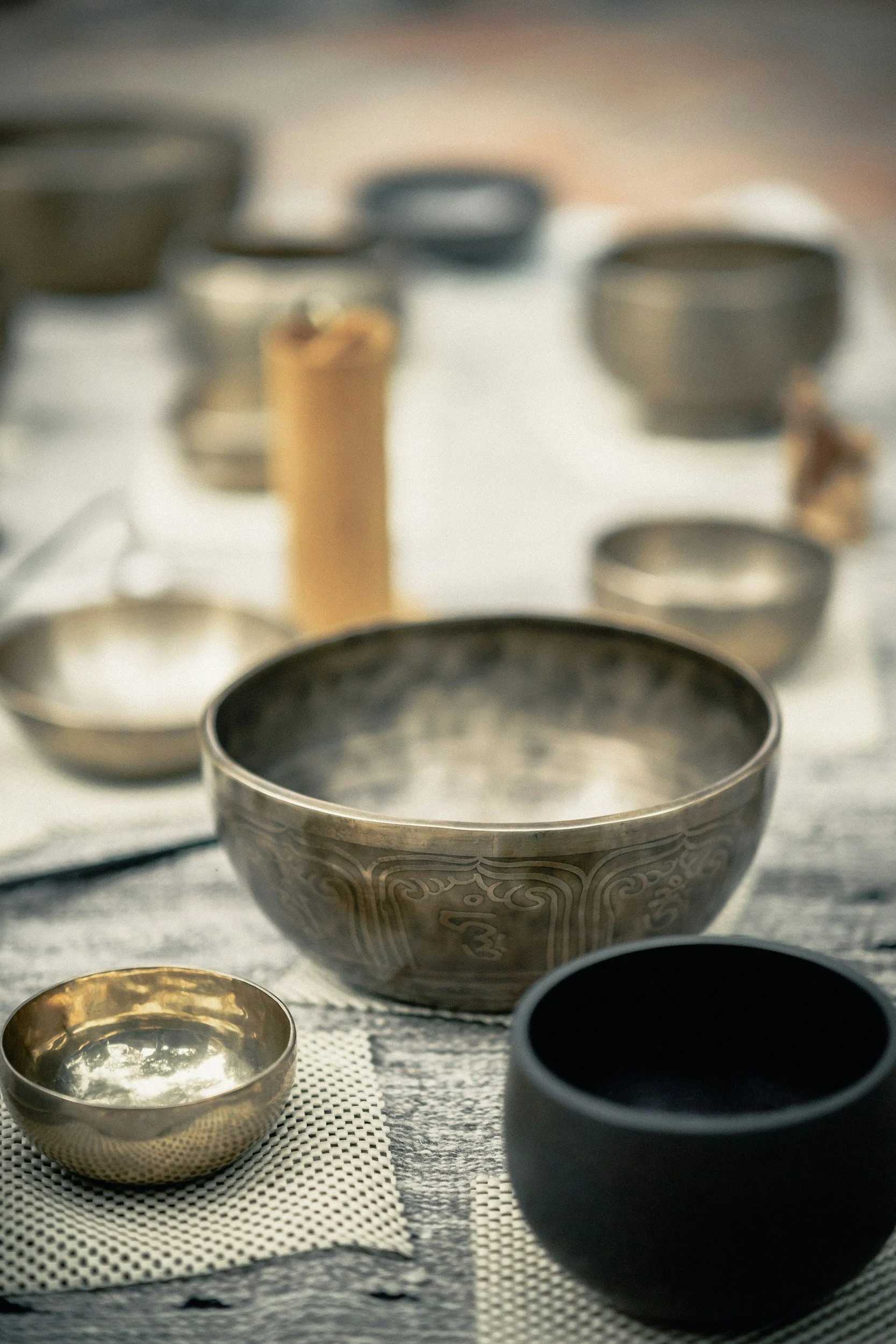 Various metal bowls and cups of different sizes arranged on a table, with a textured surface and a cloth underneath some of them.