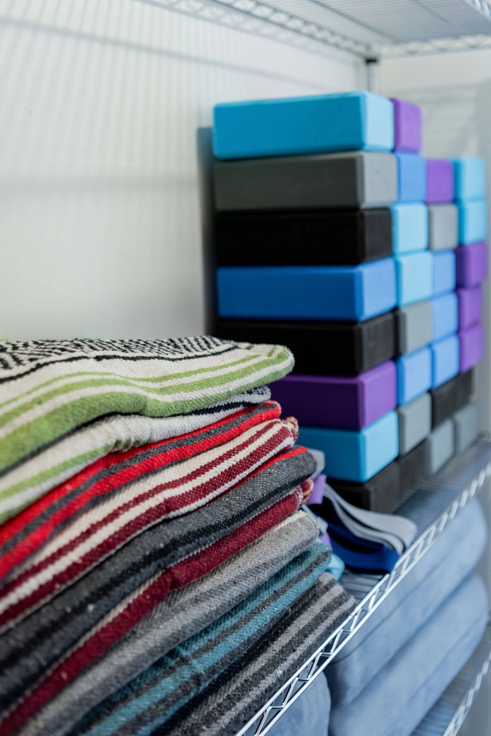 Stacked folded towels in various striped colors on a wire shelf with boxes of foam sponges in blue, black, gray, and purple in the background.