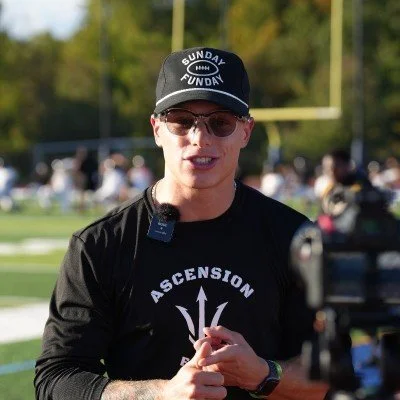 A young man with short light brown hair, smiling, wearing a blue polo shirt with a logo that says "WNE CO