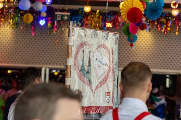 Menschen auf einer Party oder Veranstaltung, bunte Dekorationen wie Papierlampions und Girlanden, ein Banner mit Herzsymbolen und ungarischer Flagge.