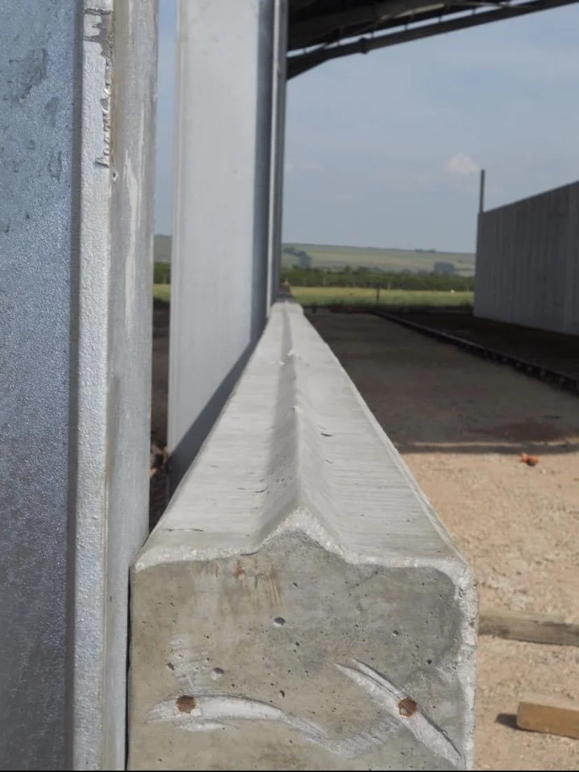 Close-up of a concrete barrier on a railroad platform with a metal structure and rail tracks, and open field in the background.