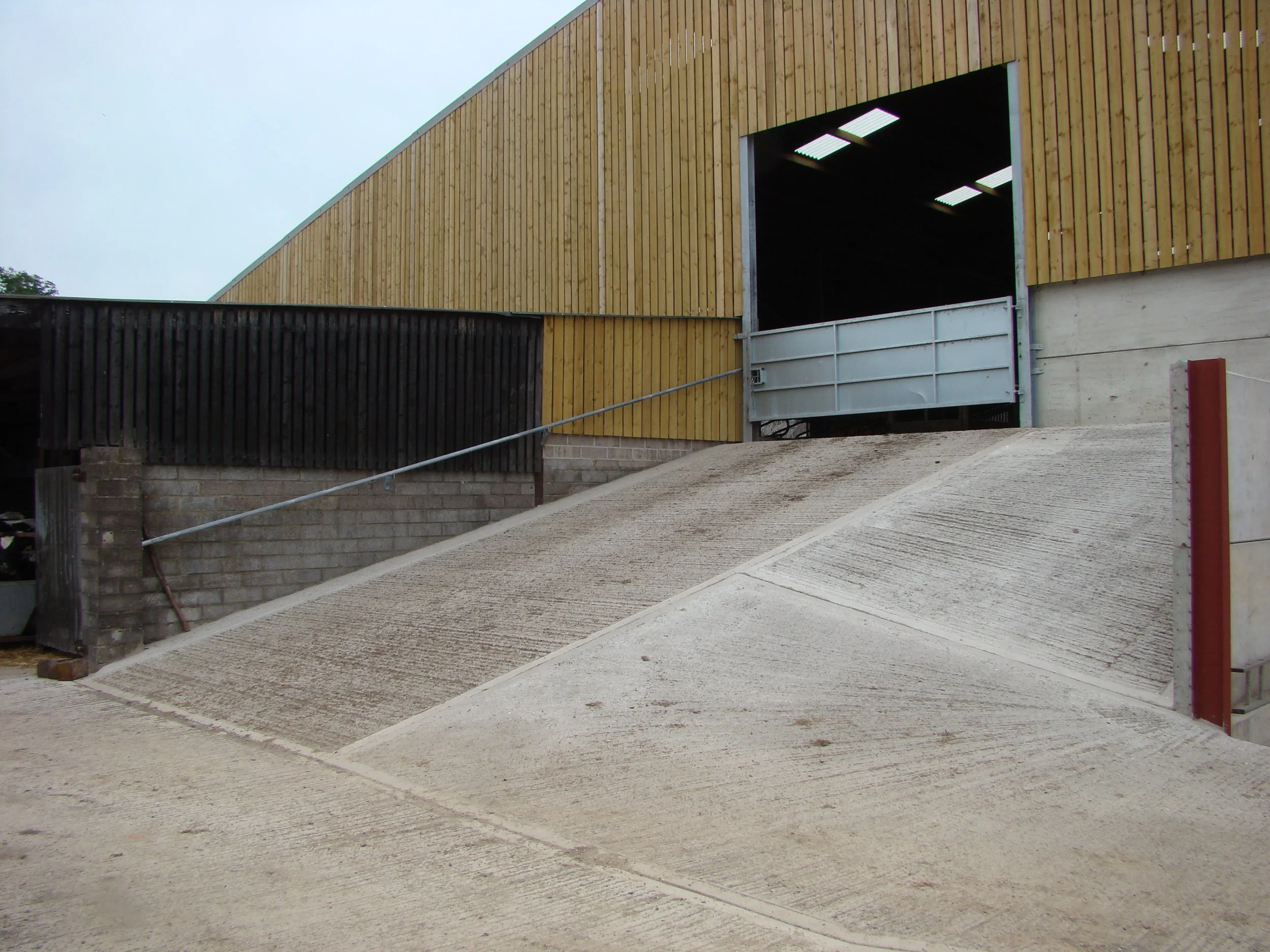 A concrete ramp leading to a large open garage with a wooden exterior wall and a metal sliding door.