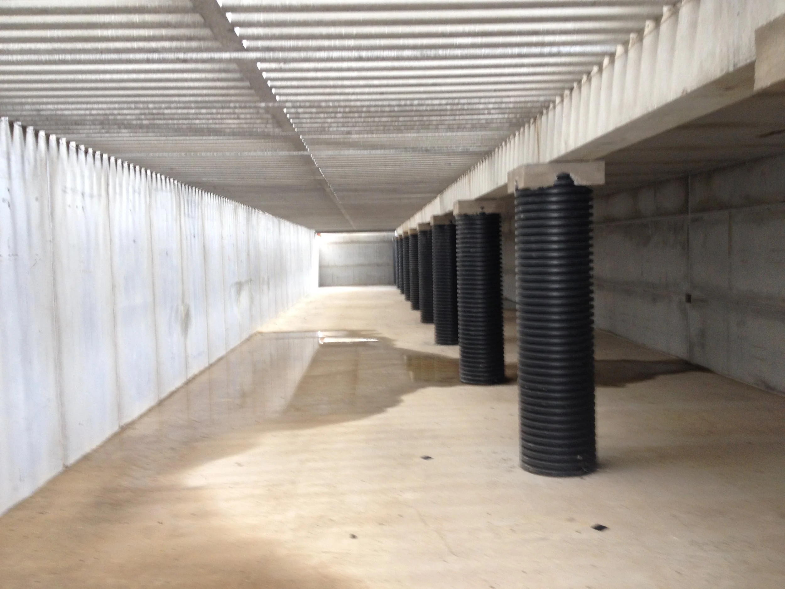 Under construction area with concrete pillars wrapped in black plastic, concrete walls, and a corrugated metal roof.