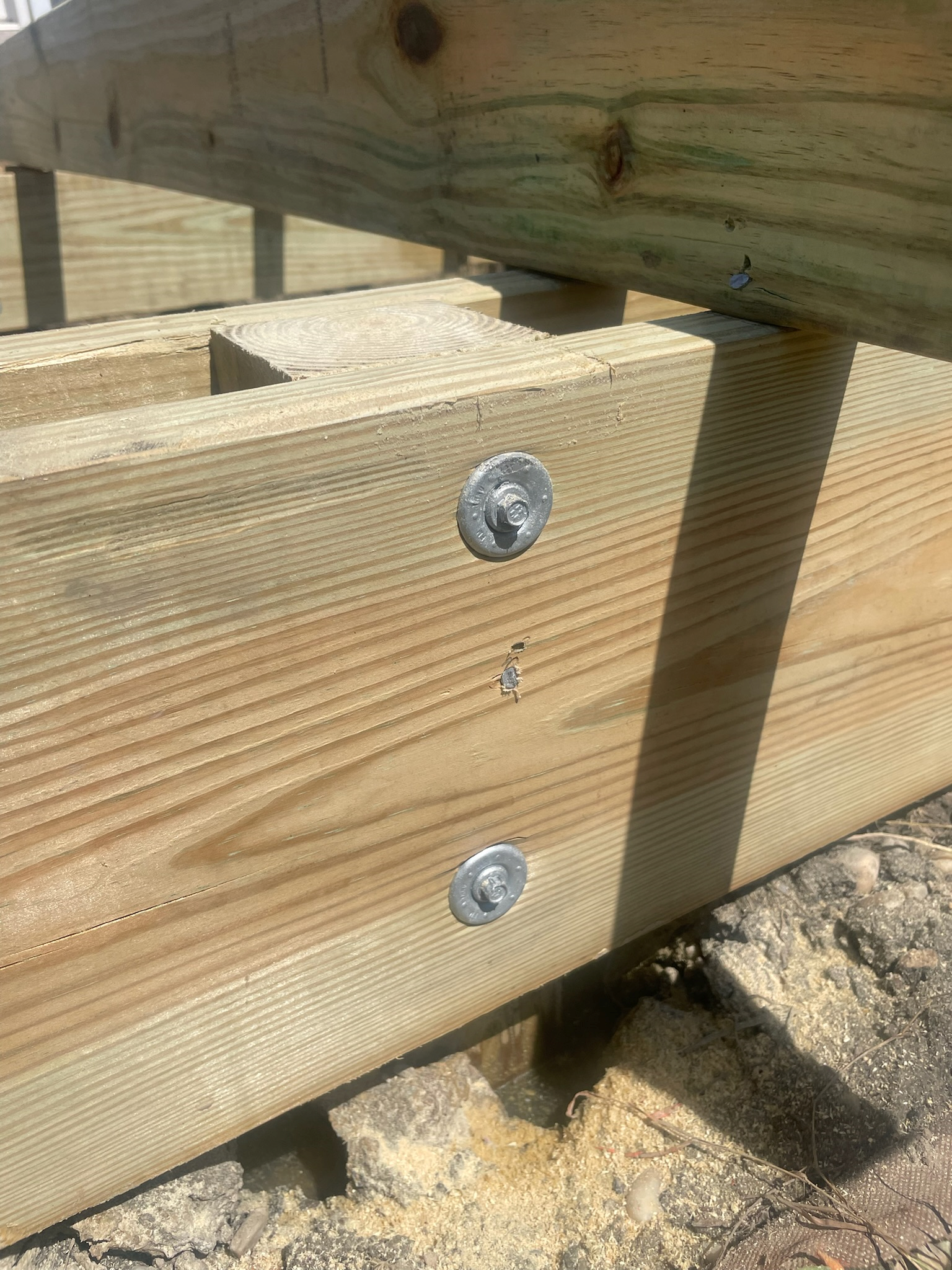 Close-up of wooden deck framing with metal bolts and nuts, showing the detail of the construction and fasteners.