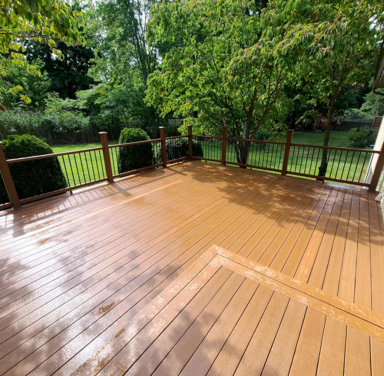 A new wooden deck with a railing, overlooking a lush green backyard with trees and bushes.