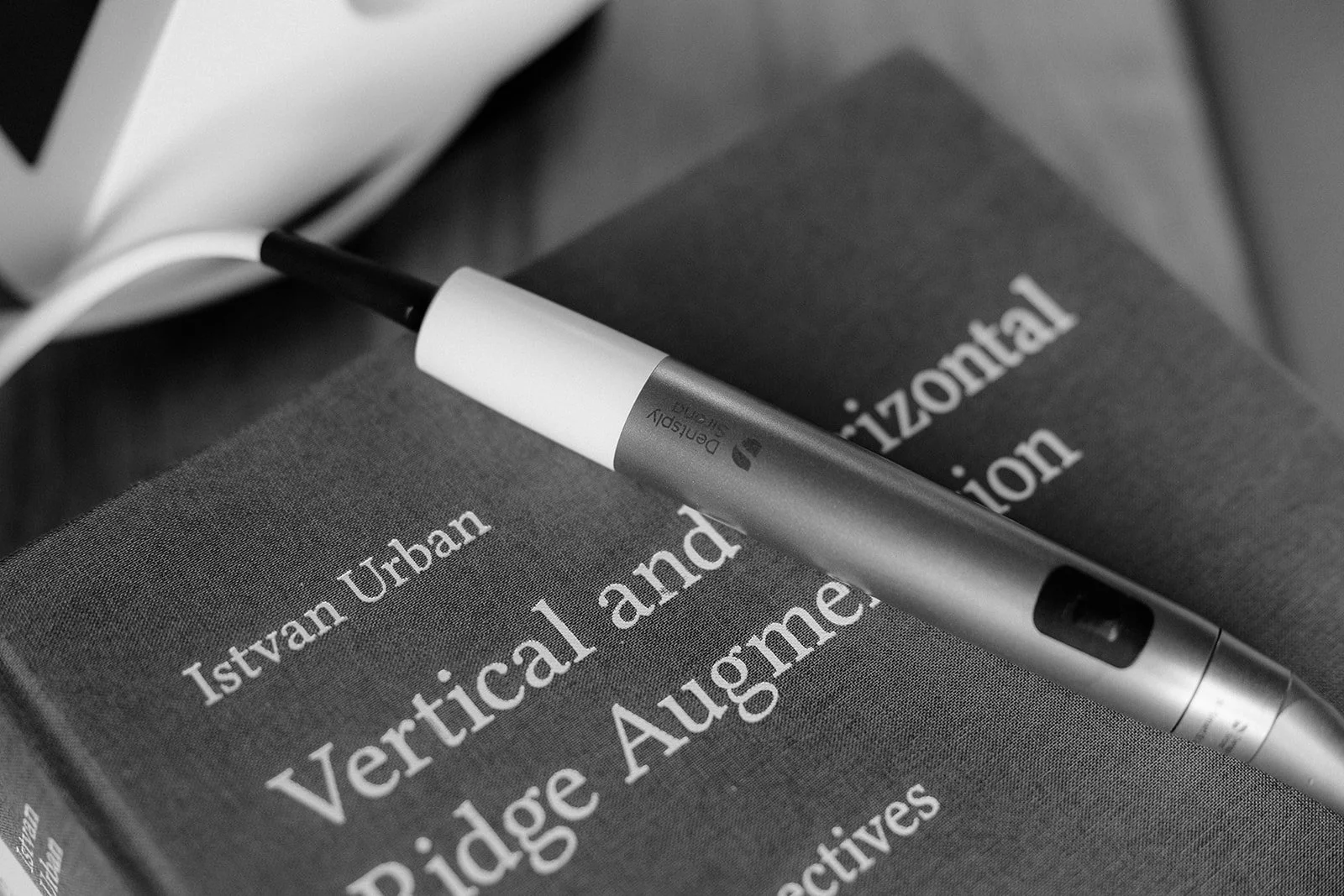 A black and white photo of a fountain pen resting on two academic books, one titled "Urban" and the other "Vertical and" by Rüdige August, with a laptop in the background.