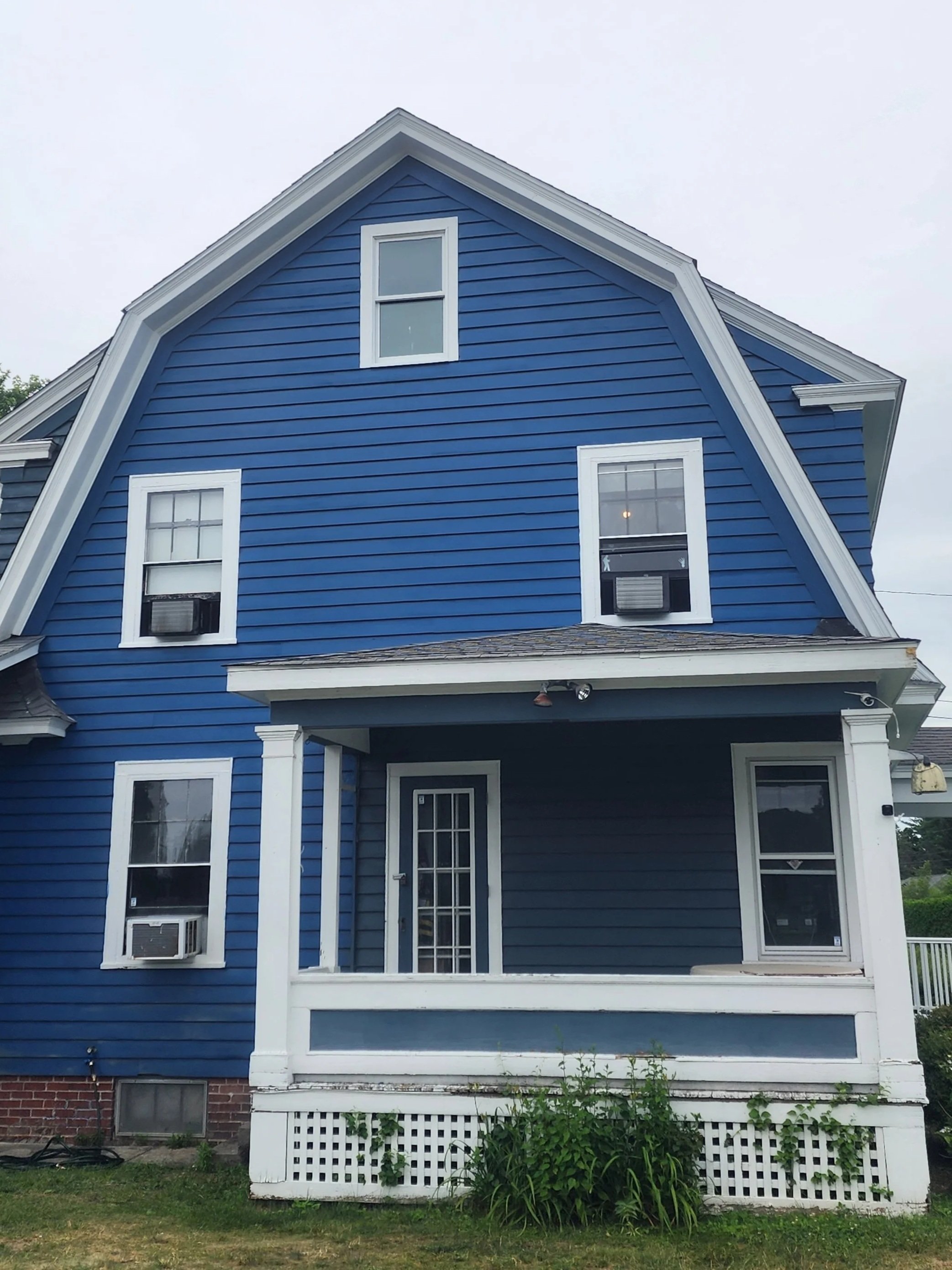 A blue Victorian-style house with white trim, three stories, multiple windows, and a small porch with a white railing.