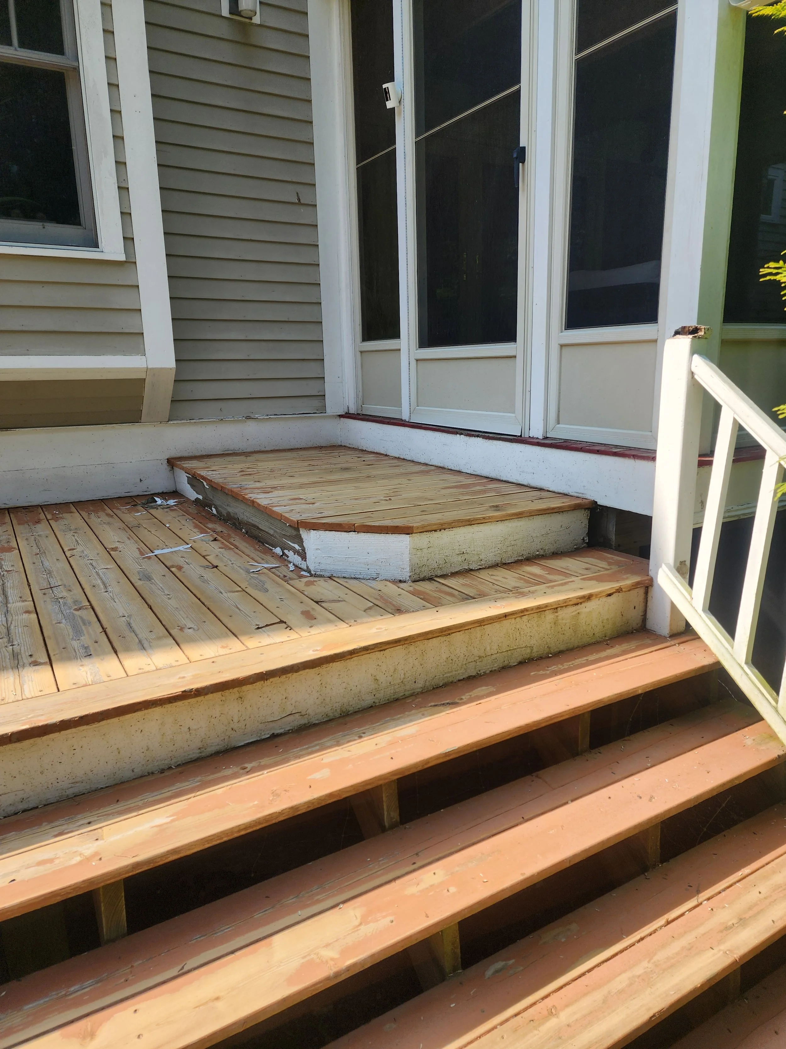 Outdoor wooden deck in construction, with new wooden planks installed on the upper section and stairs leading up to a sliding glass door.