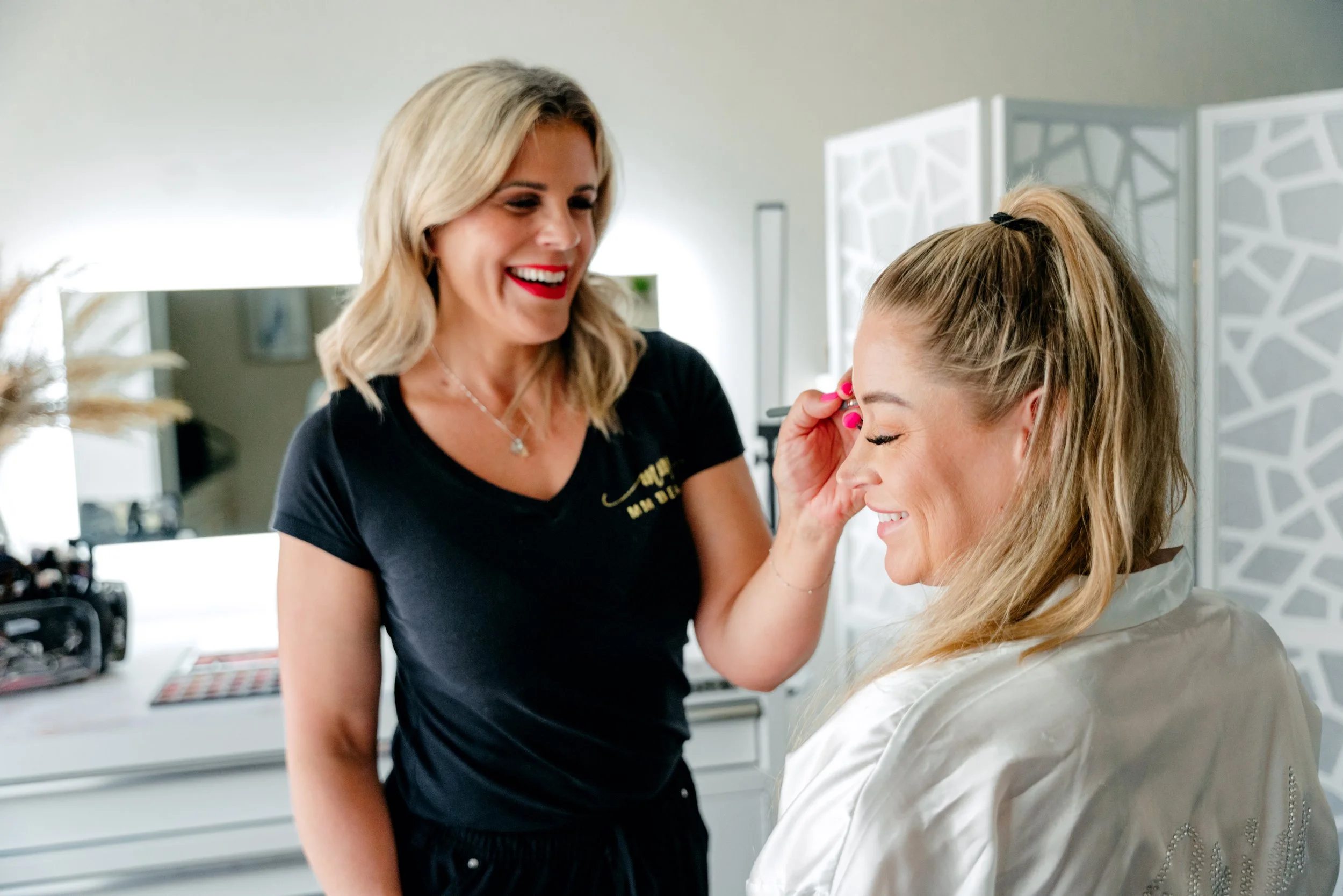 Makeup artist applying makeup to a smiling woman in a beauty studio.