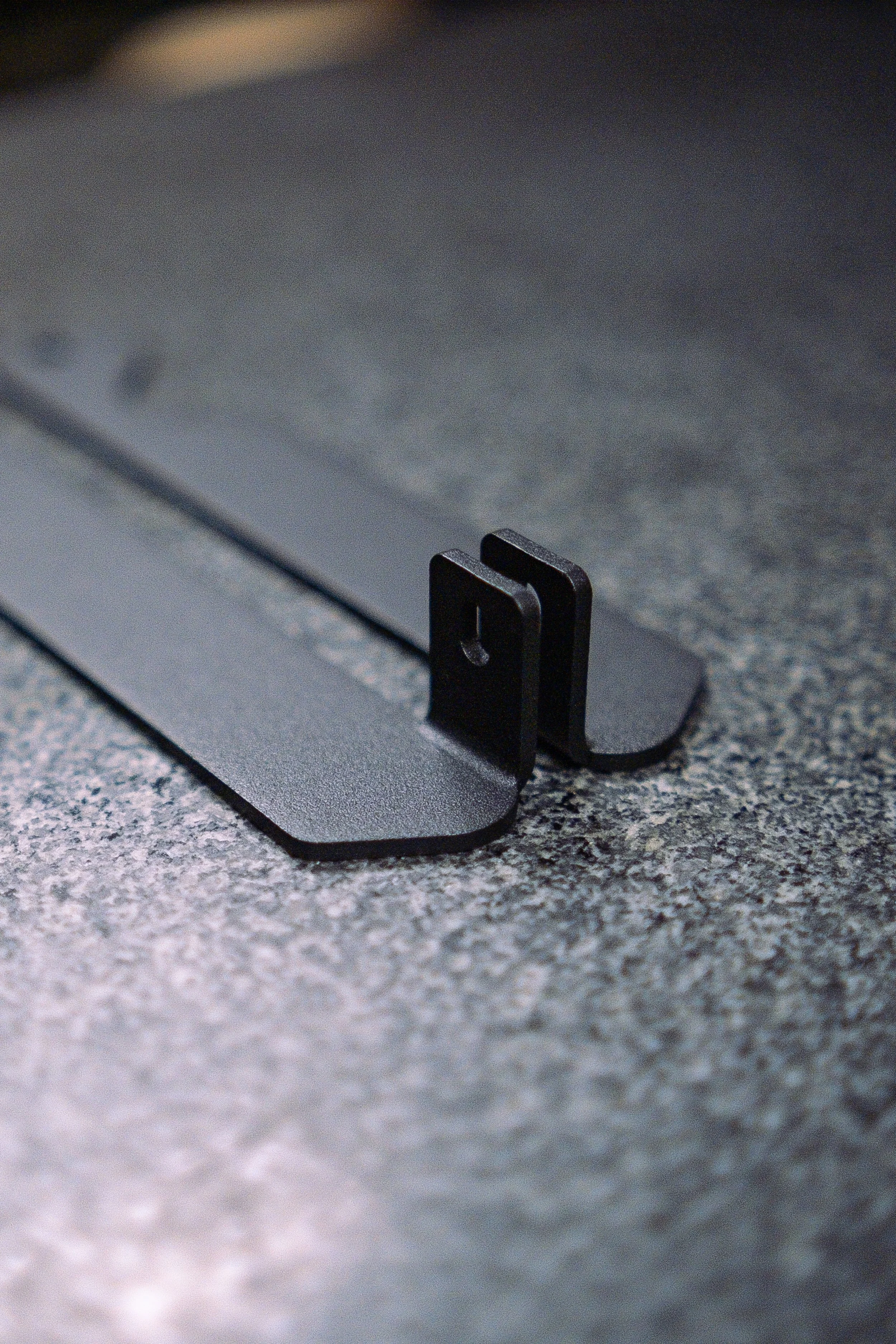 Disassembled black metal and plastic car roof rack mounting brackets with screws and spacers on a gray surface.