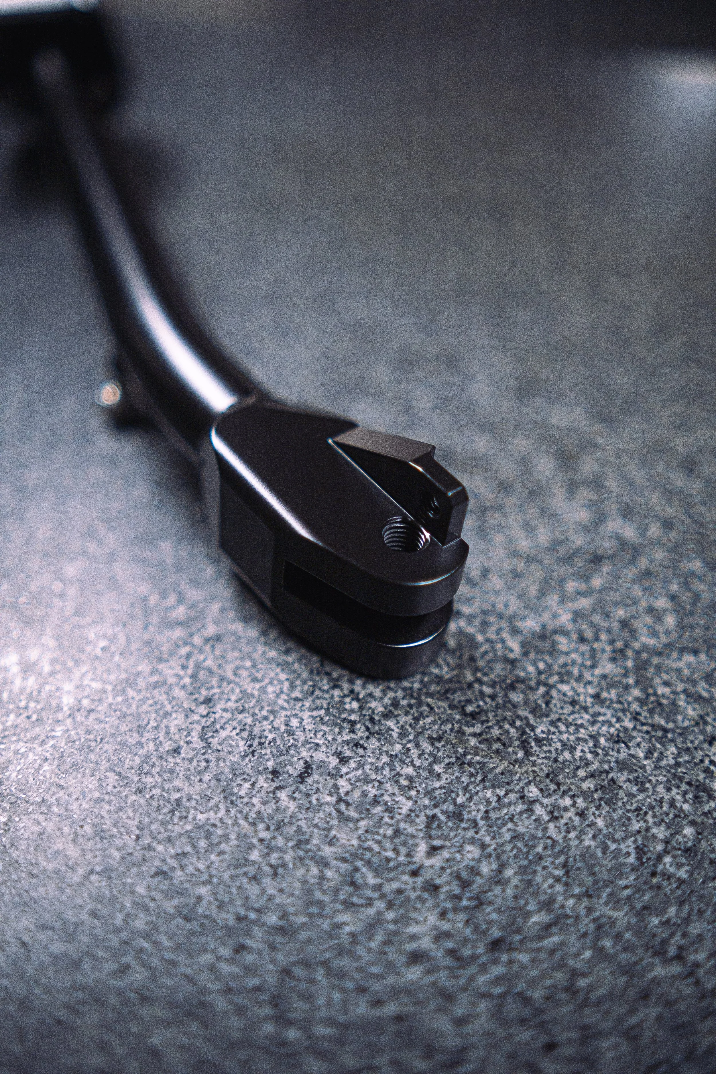 Close-up of a black mechanical rail clip with a brass screw, resting on a textured dark gray surface.