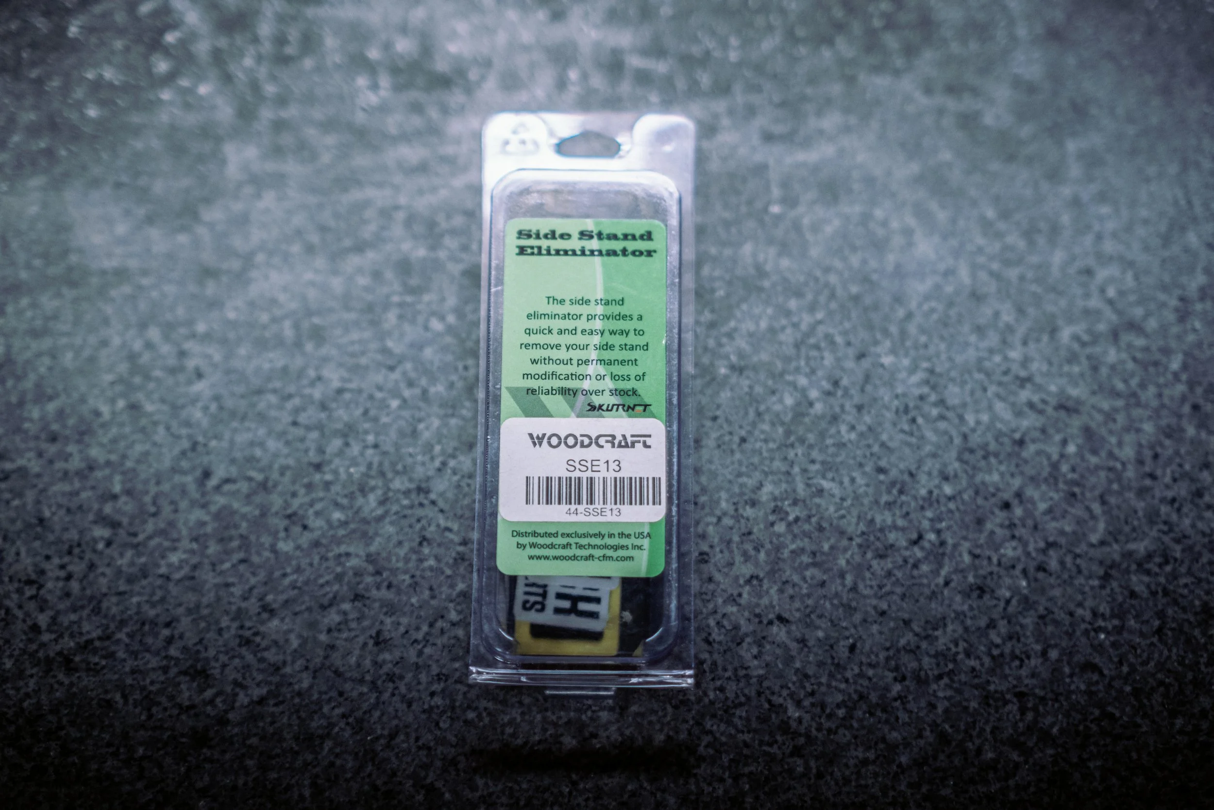 Packaging for a Woodcraft side stand eliminator, labeled with product details, barcode, and company information, placed on a dark textured surface.