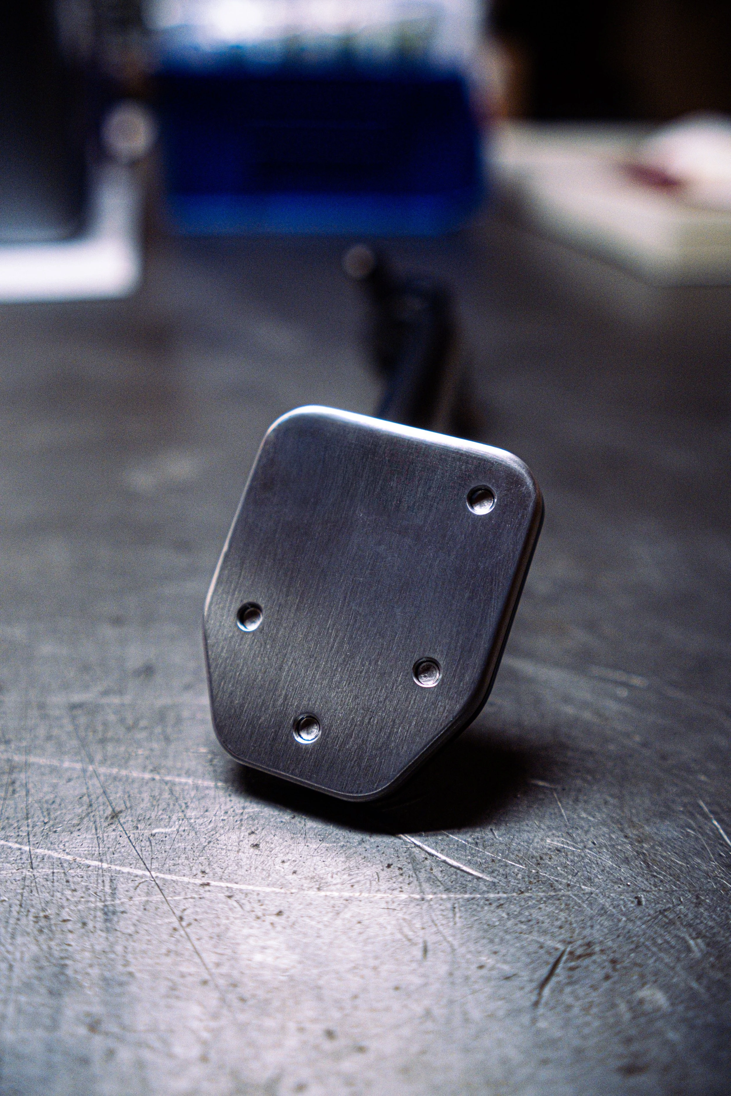 Close-up of two black metal motorcycle foot pegs with silver screws on a rough gray surface.