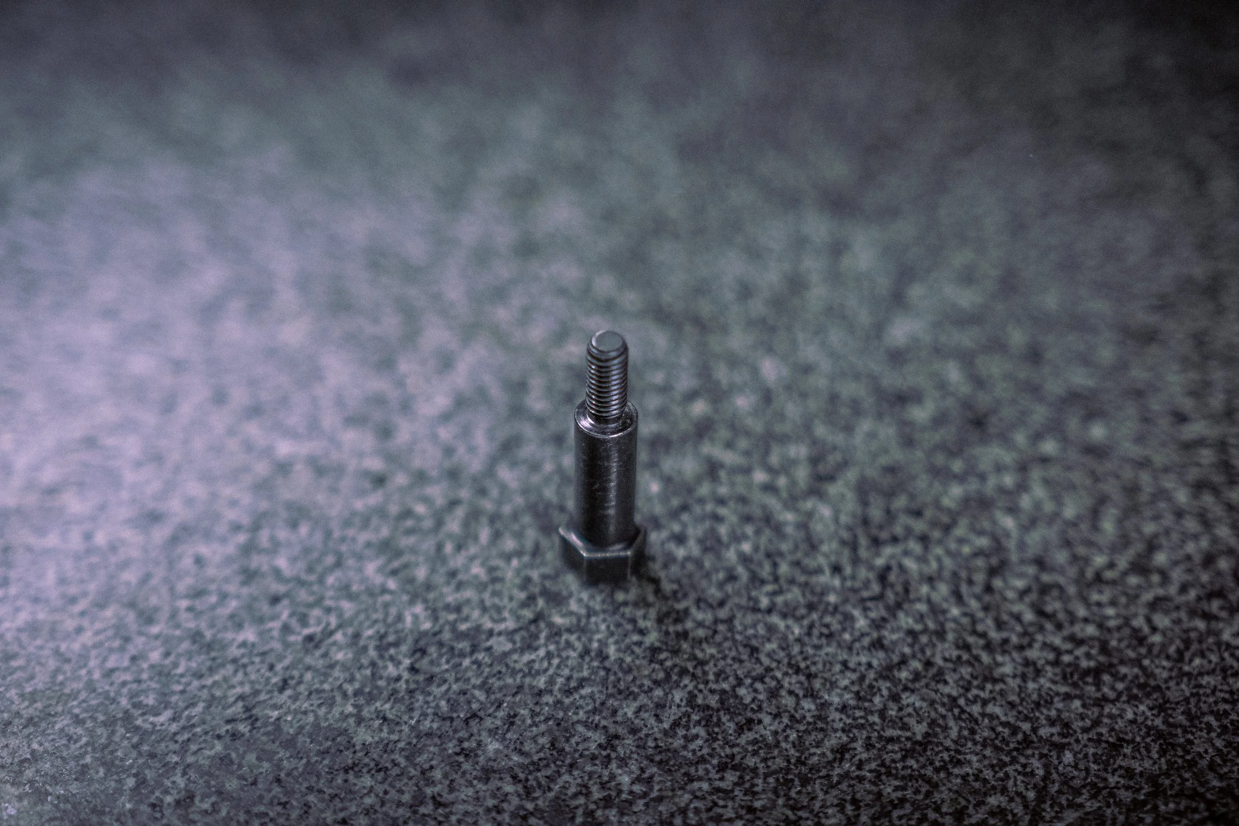 A small metal bolt standing upright on a textured dark surface.