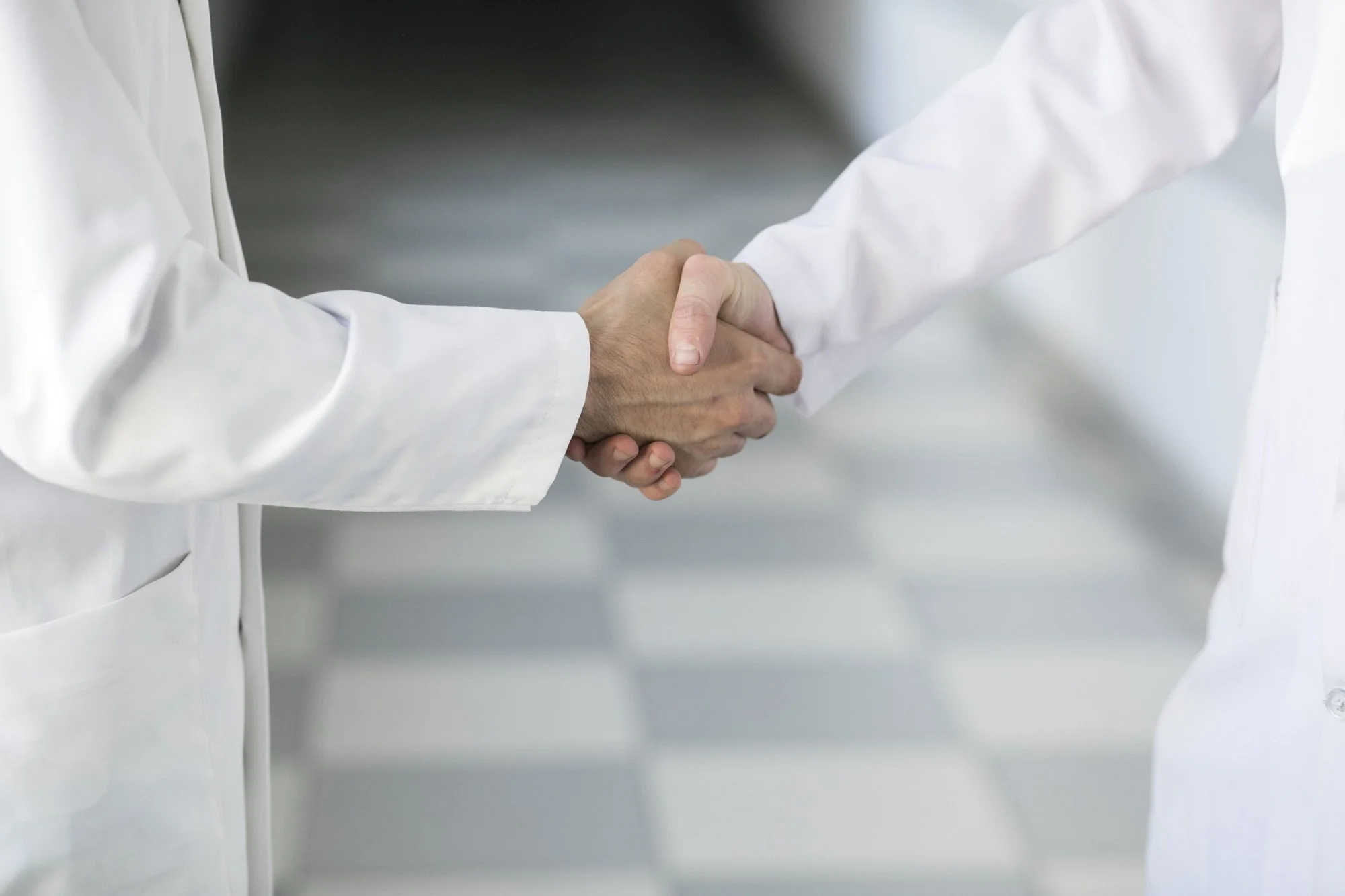 Two healthcare professionals wearing white coats shaking hands in a medical setting.