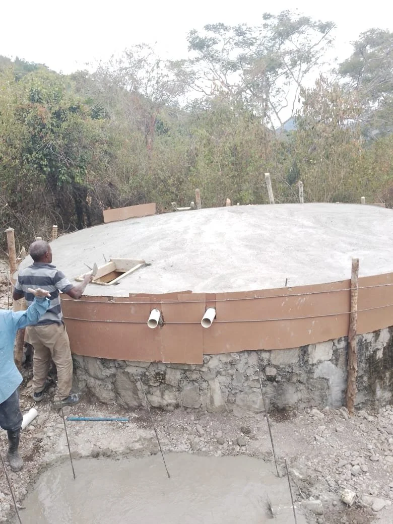 Construction workers building a round concrete structure in a wooded area.