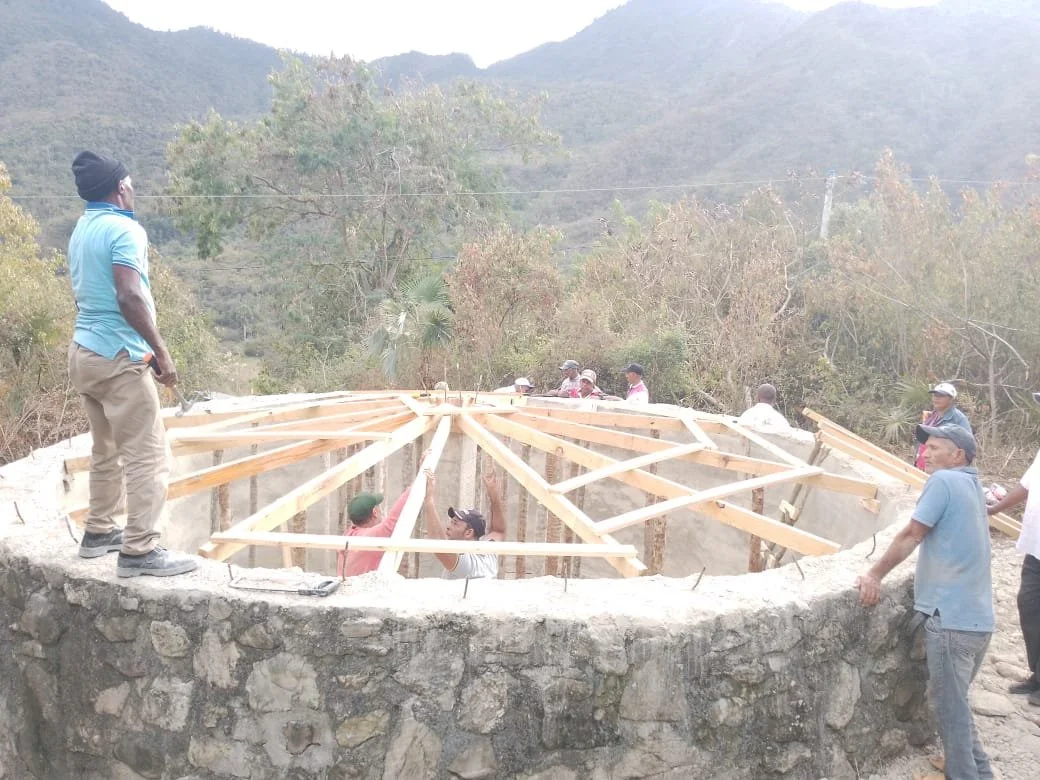 Group of people constructing a wooden frame on a stone structure outdoors.