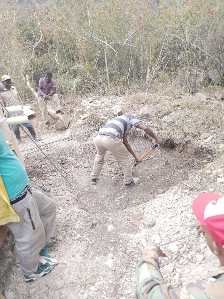 Men working on outdoor construction project in a rural area, surrounded by rocky terrain and sparse vegetation.
