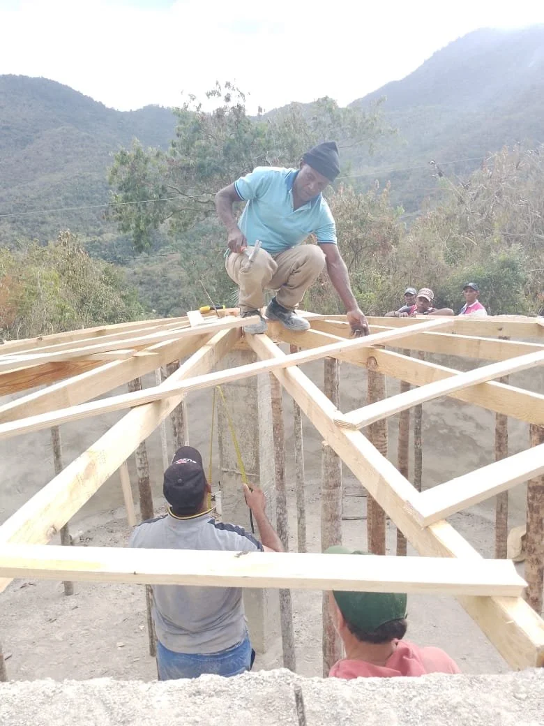 Construction workers building a wooden roof structure in a mountainous area.