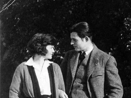 A black and white photo of a man and woman standing close to each other outdoors, looking into each other's eyes.