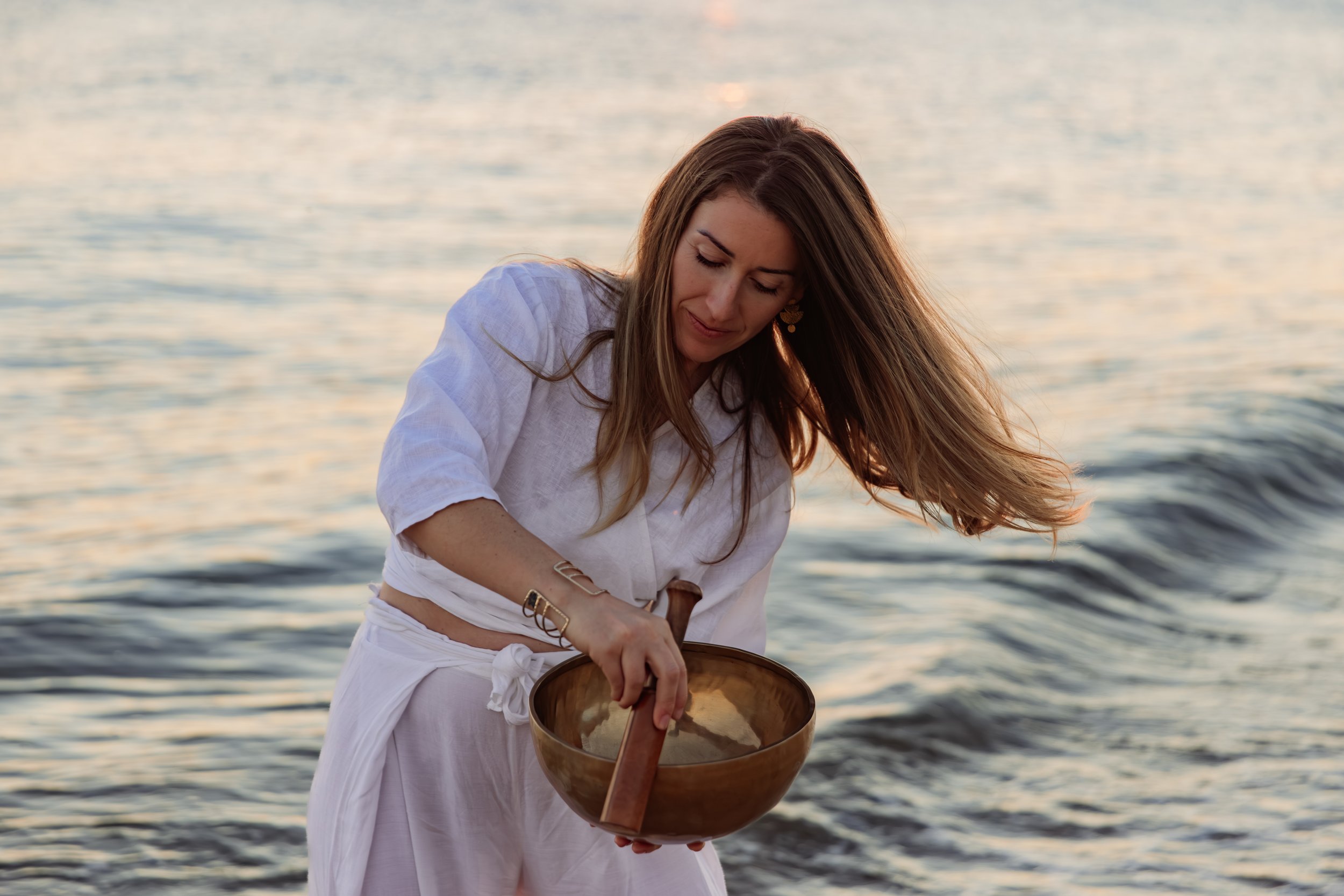 Une femme qui joue d'une cymbale en métal près de la mer au coucher du soleil.