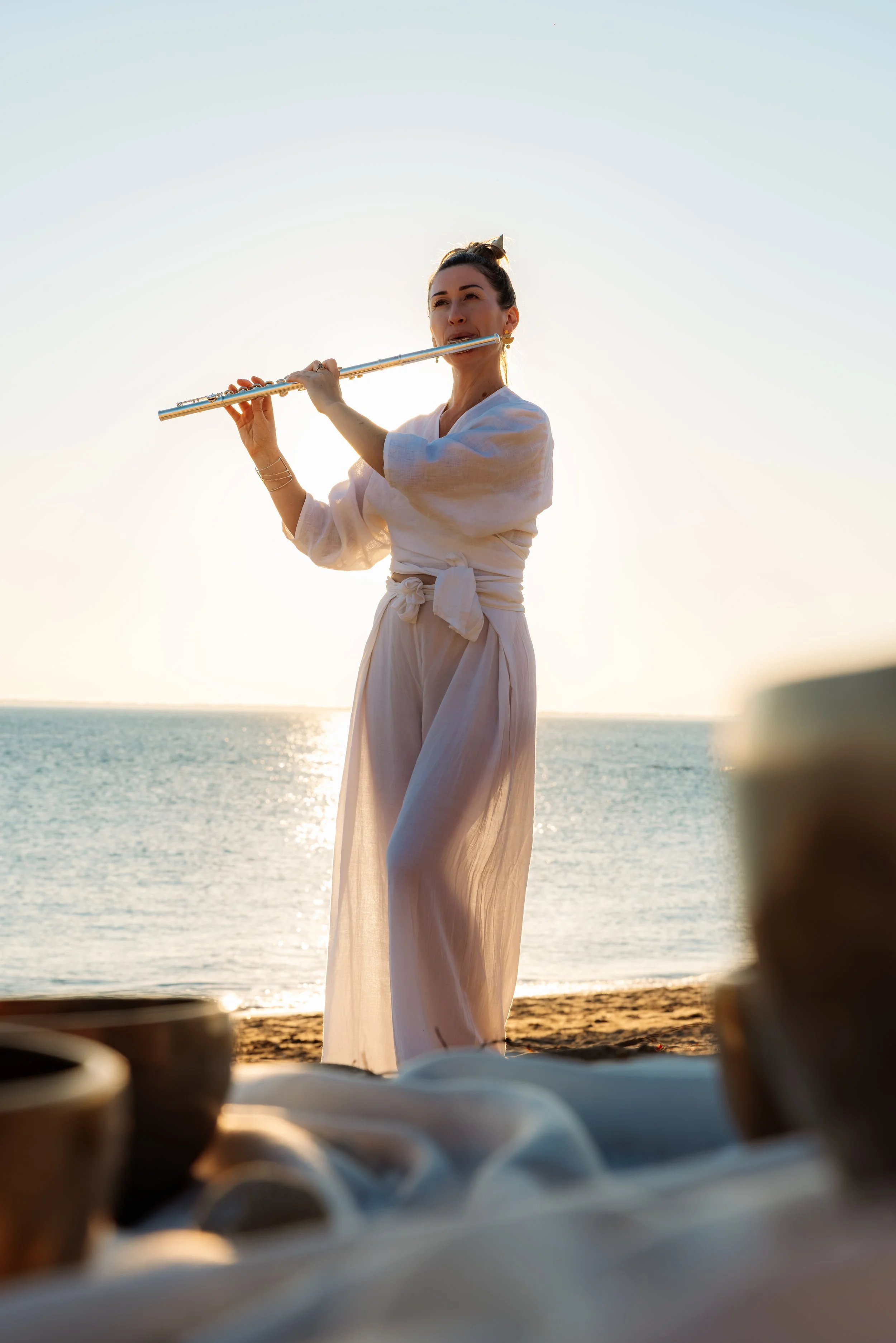 Une femme joue de la flûte à la plage au coucher du soleil.