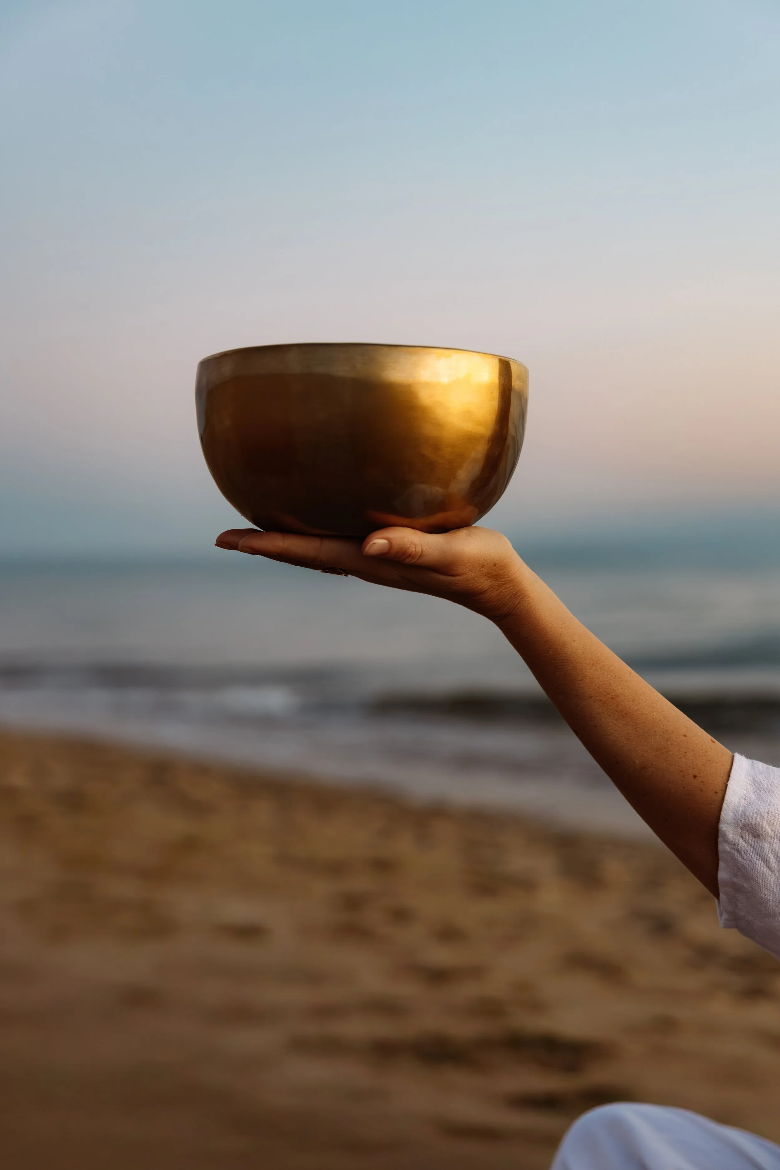 Une main tient un bol en métal brillant devant une plage au coucher du soleil