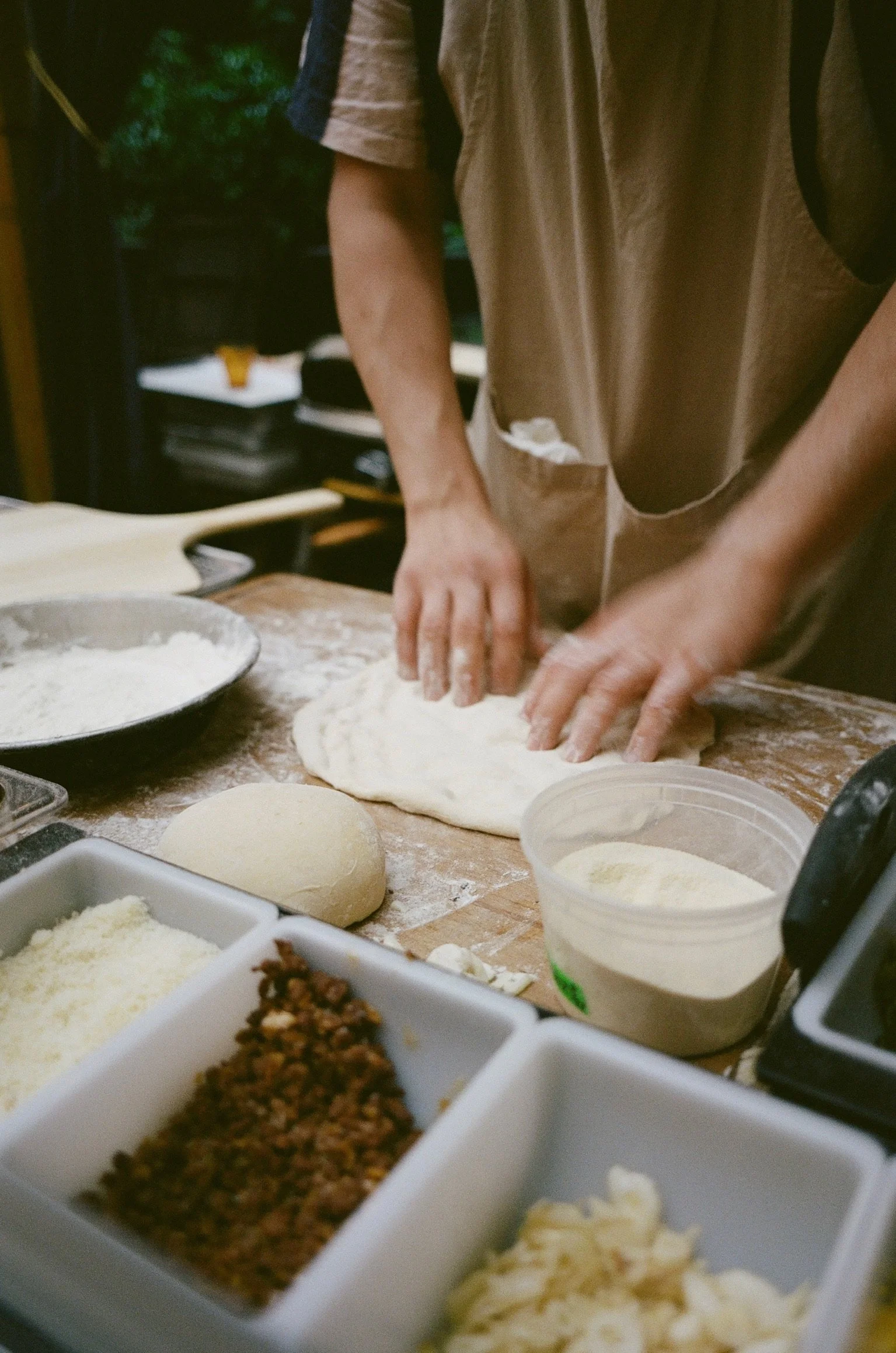 Person making pizza dough at a kitchen counter with bowls of ingredients.
