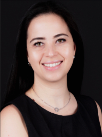 A young woman with long dark hair smiling, wearing a black sleeveless top and a necklace, against a dark background.