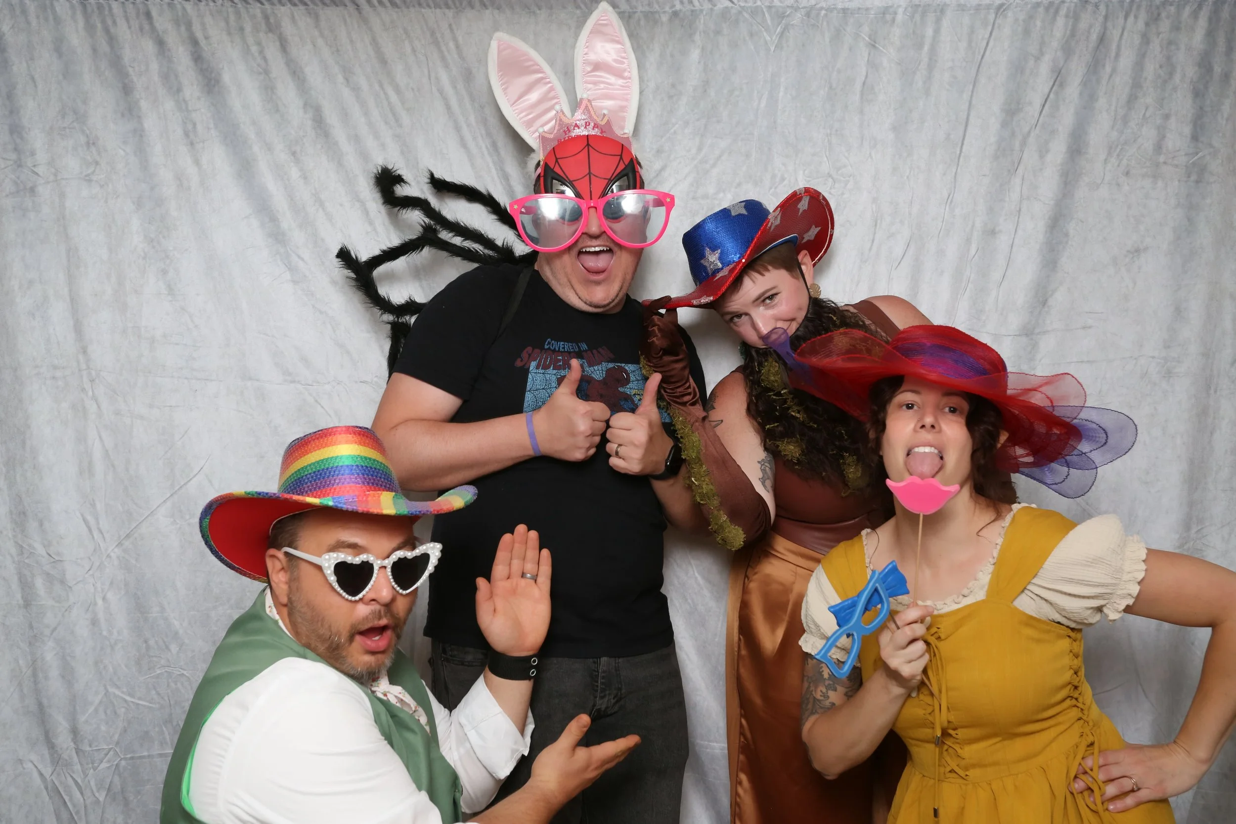 Group of five people in festive costumes and masks posing playfully in front of a plain backdrop.