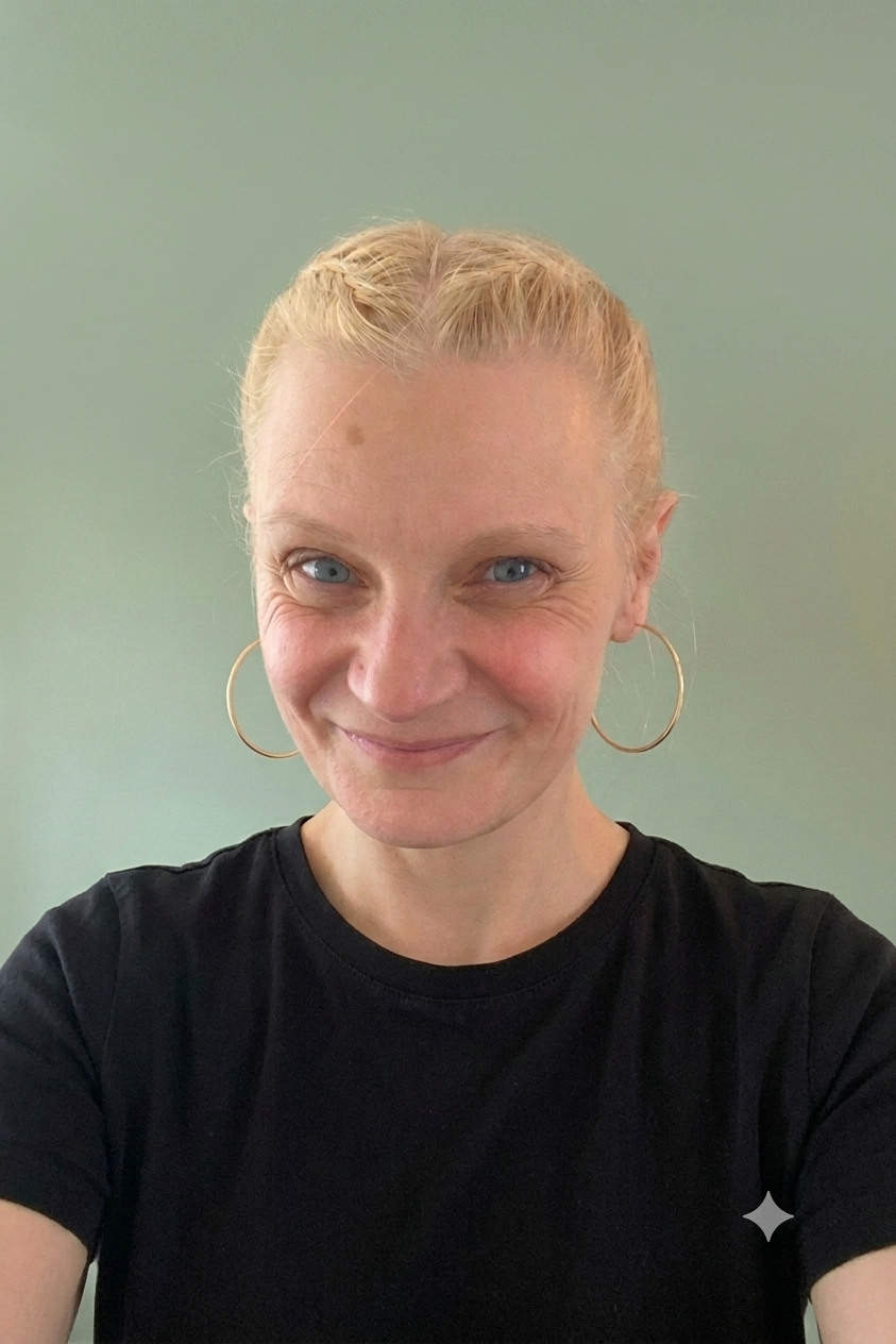 A woman with blonde hair in a braid, wearing large hoop earrings and a black shirt, smiling against a plain, light green background.