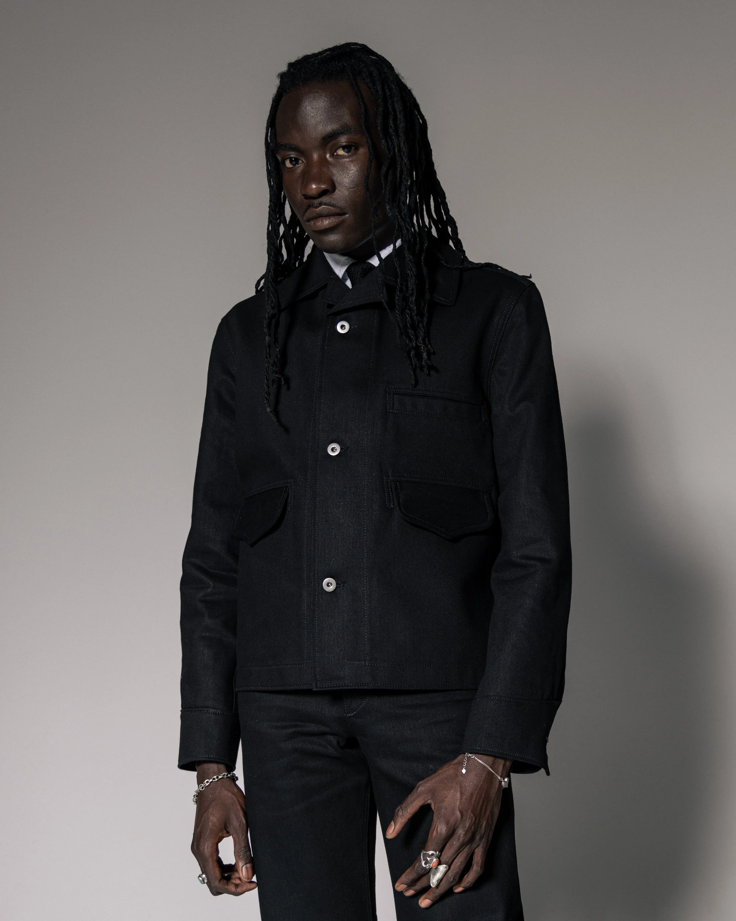 Person wearing a stylish black jacket and pants, standing against a neutral background.