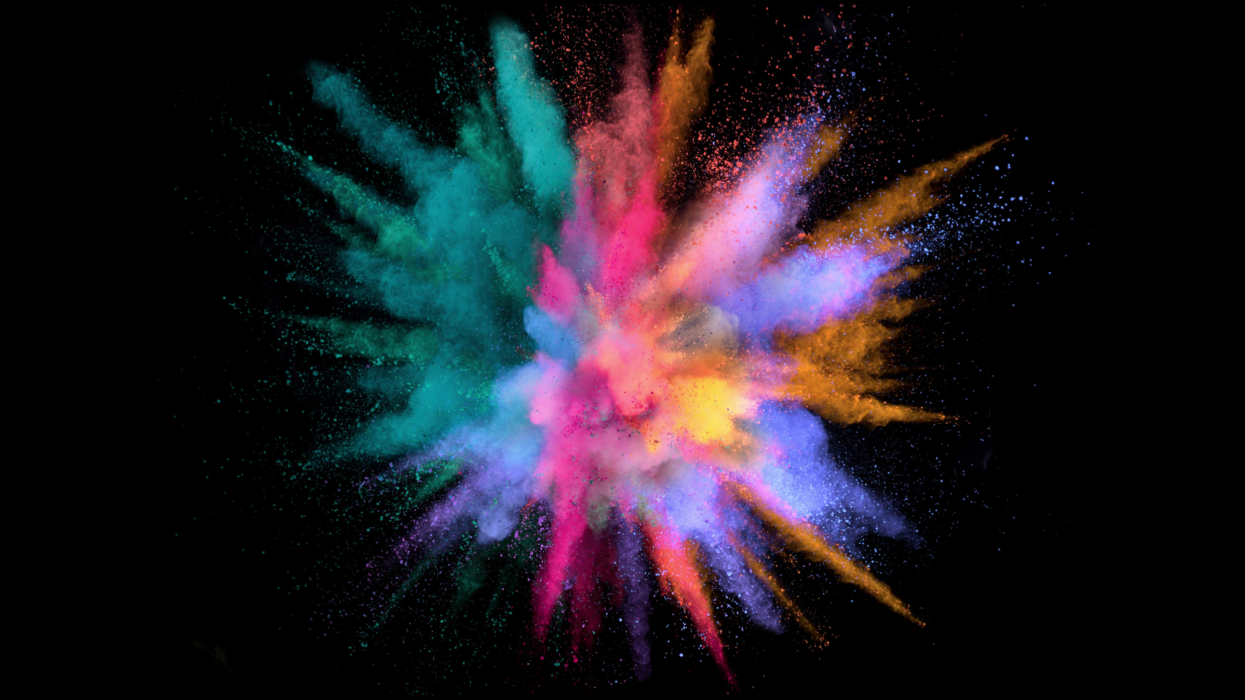 Un'esplosione di polvere colorata, con sfumature di blu, rosa, arancione, giallo e viola, su sfondo nero.