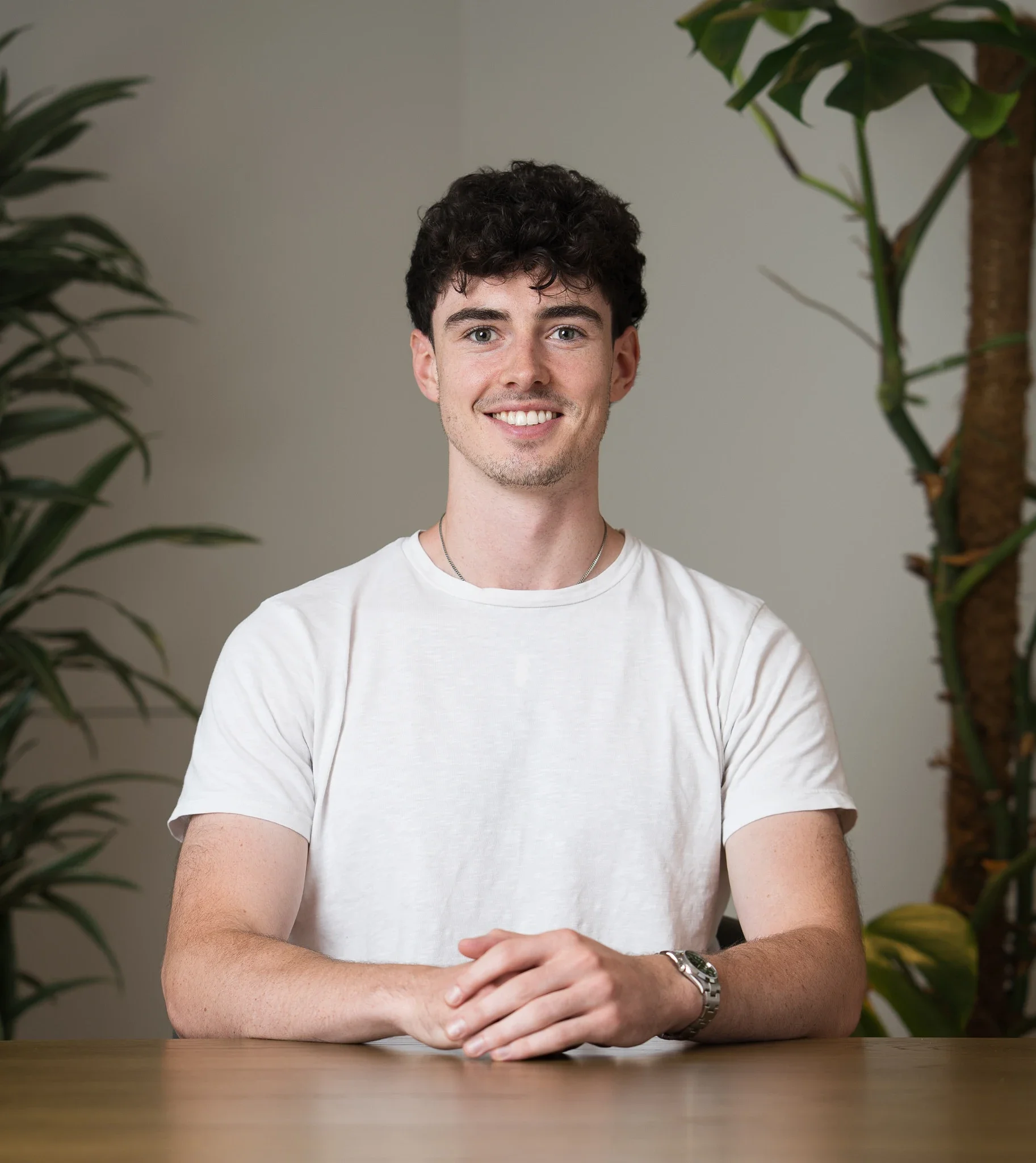 Male business headshot, neutral background with plants, casually dressed