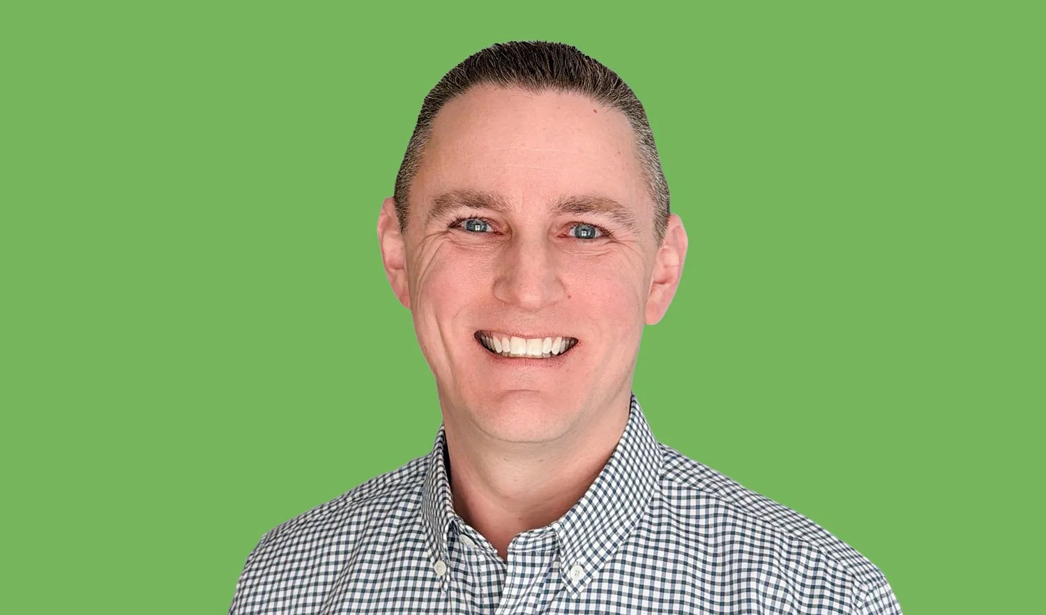 Portrait of a smiling man with short dark hair, blue eyes, wearing a purple plaid shirt, against a solid green background.