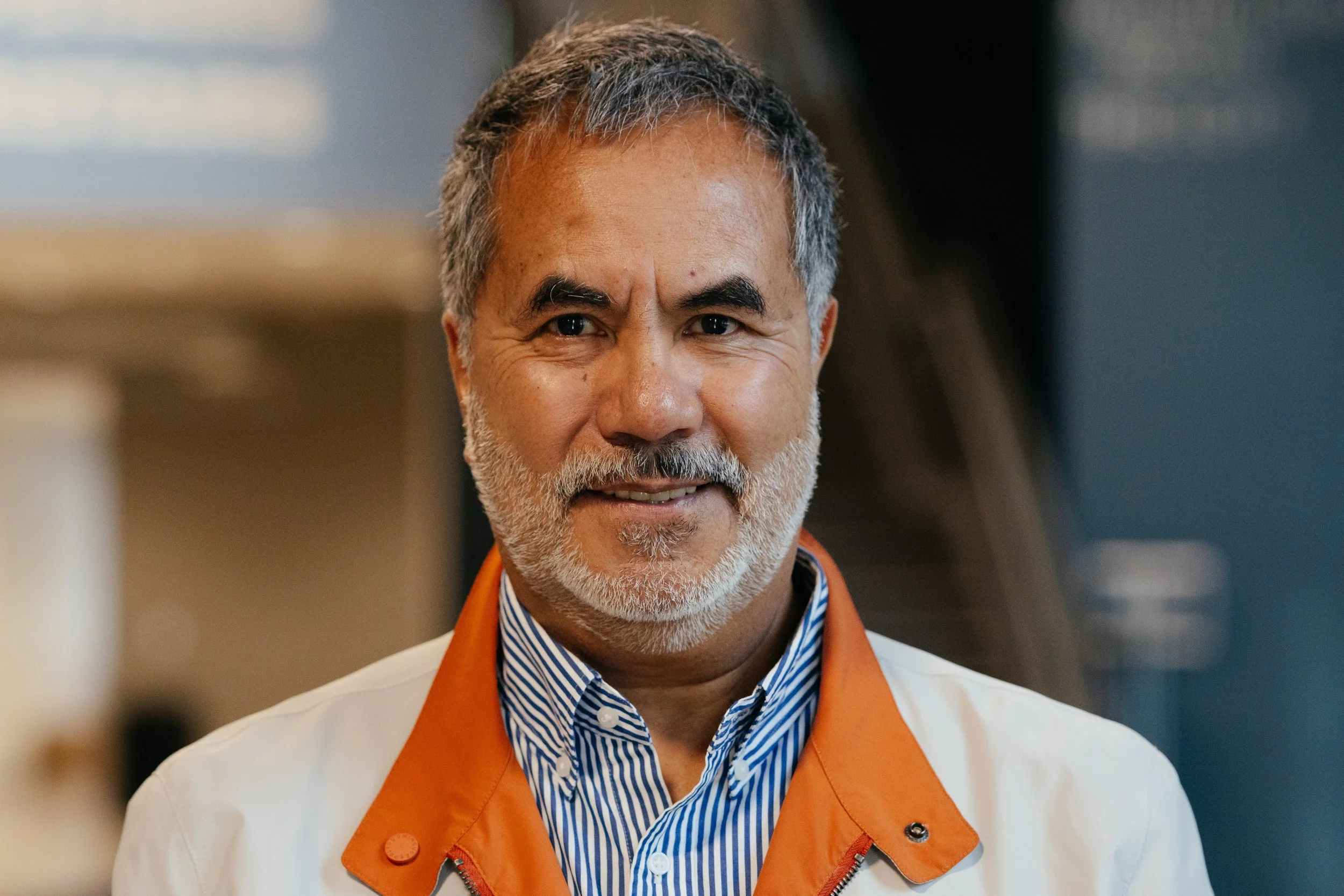 A smiling middle-aged man with gray hair against a background of green trees and water.