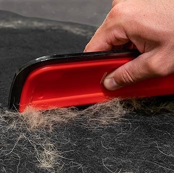 Person using a brush to remove pet fur from a black fabric surface.