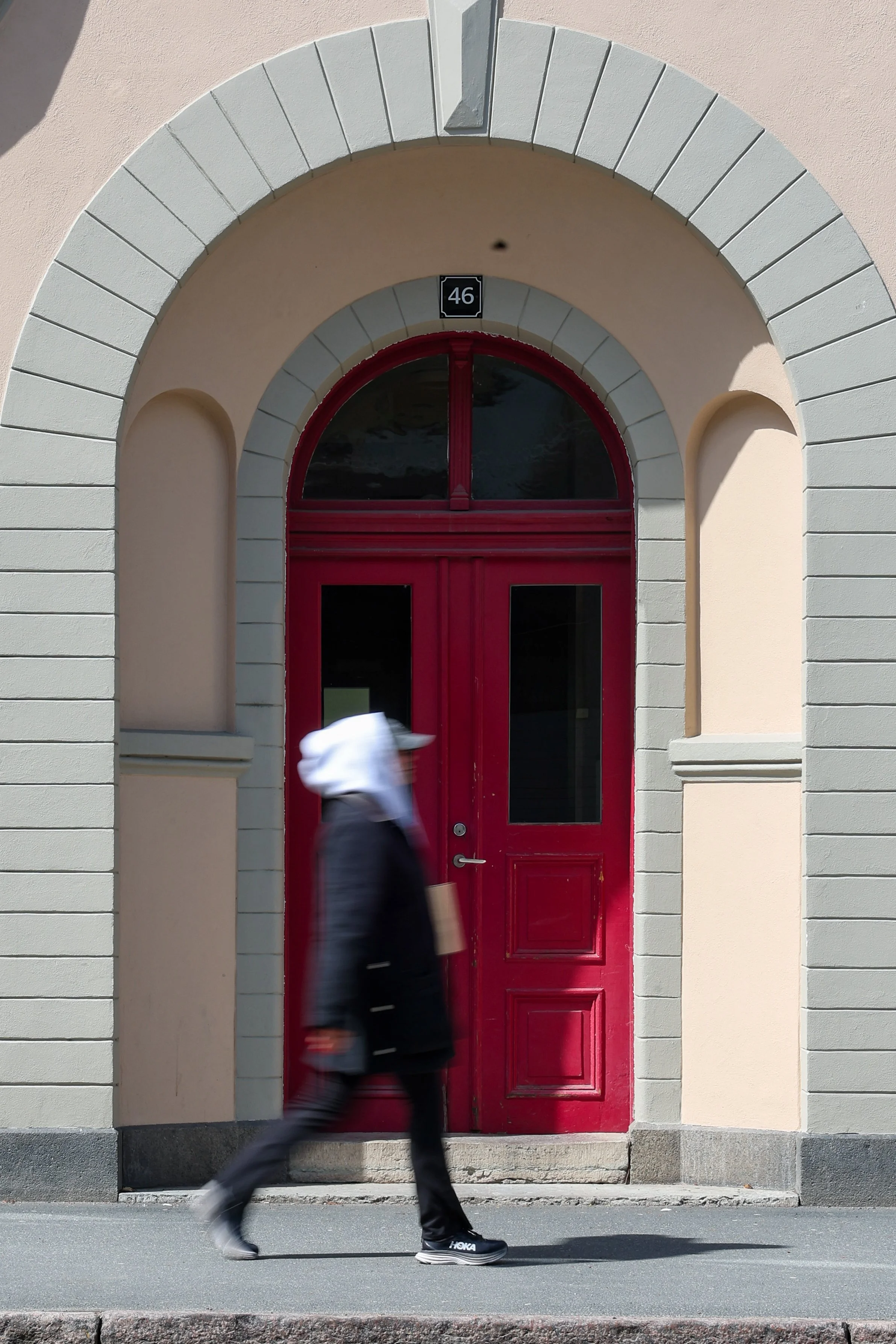 Person går förbi ett rött dörr och ett inramat nummer 46 över dörren på en beige byggnad.